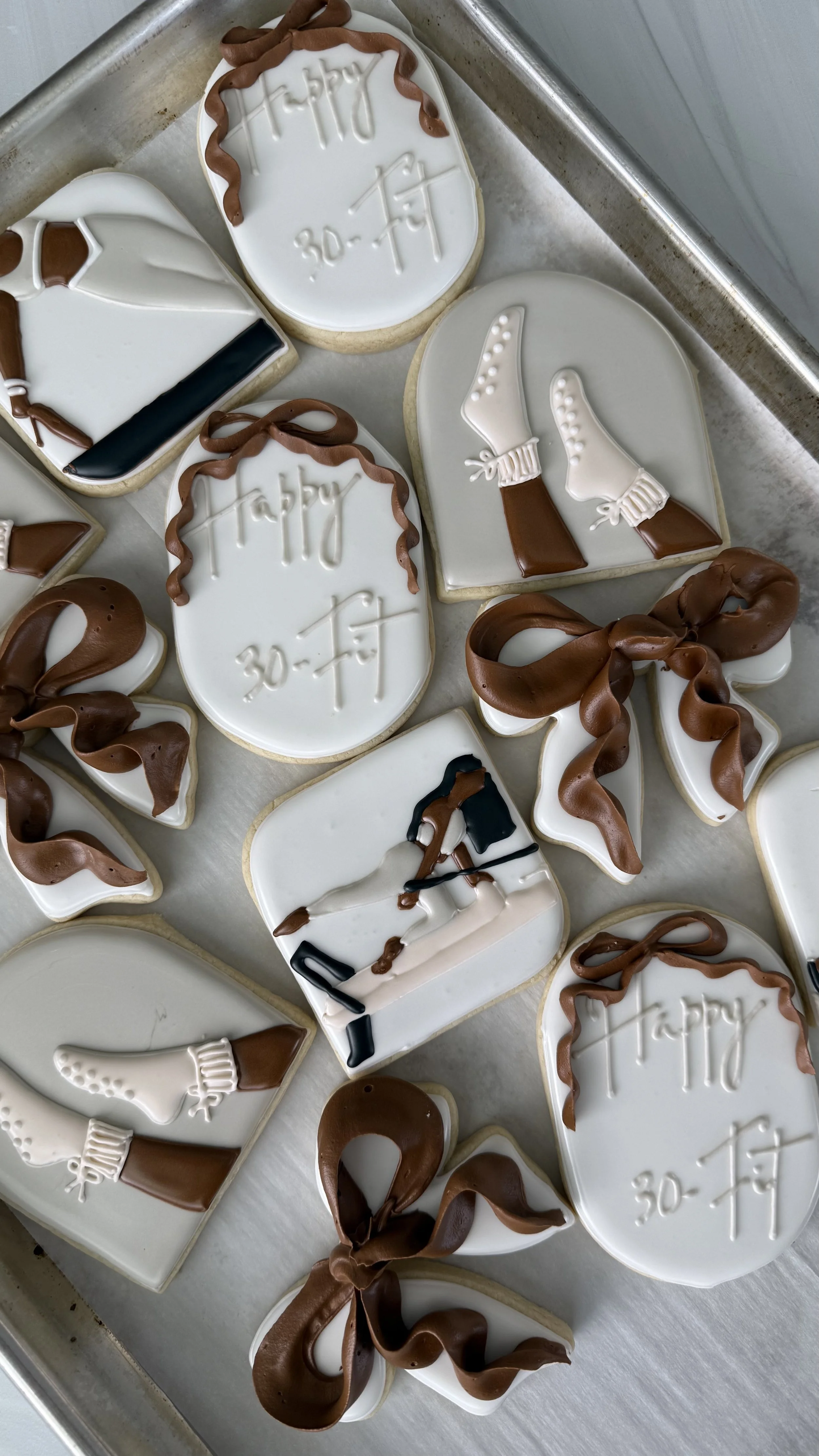 Cookies decorated with white and brown icing, some with the words "Happy 30th" and others with ice skates, all on a tray.