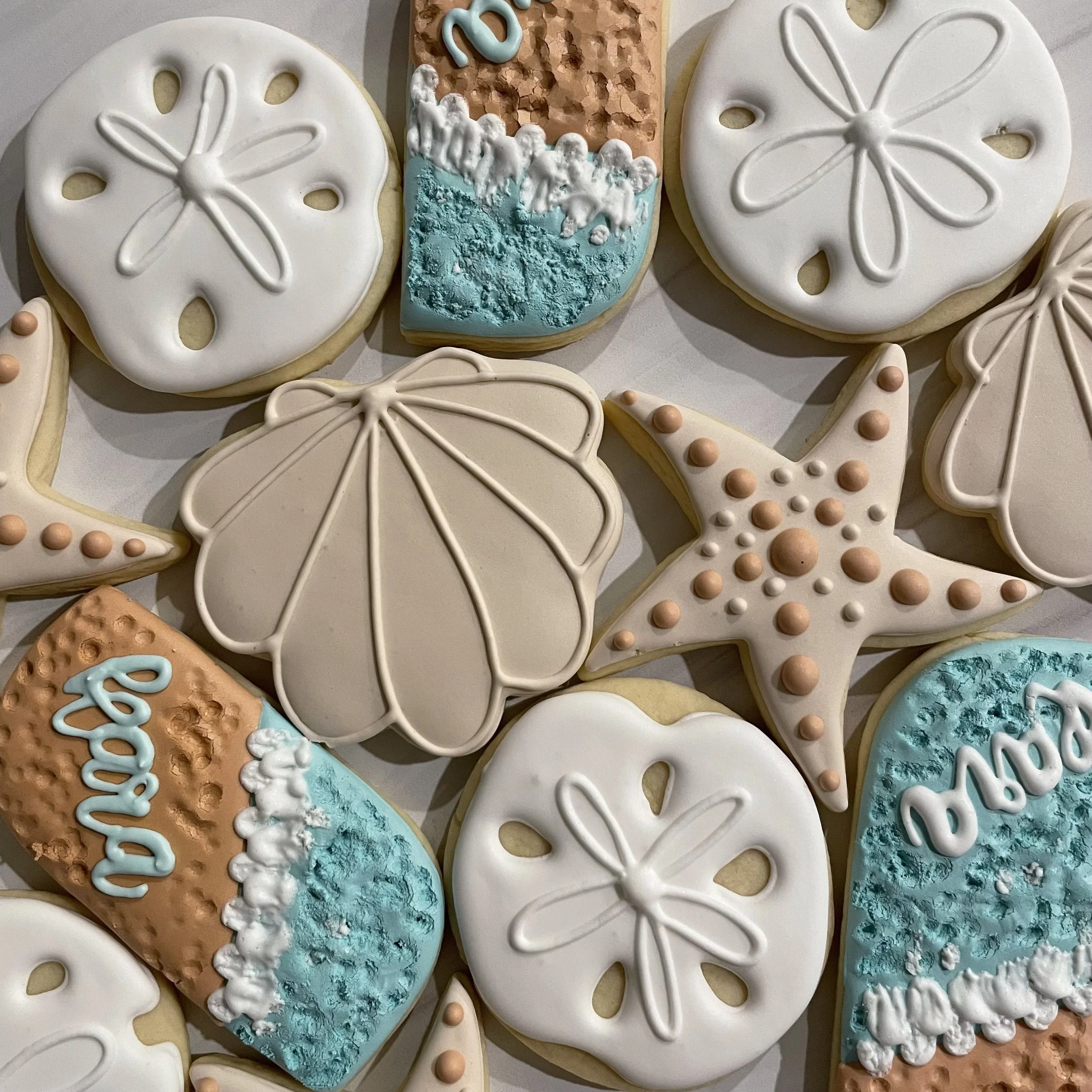 Decorated cookies in butterfly, snowflake, and abstract styles with white, blue, and tan icing and pearl accents.