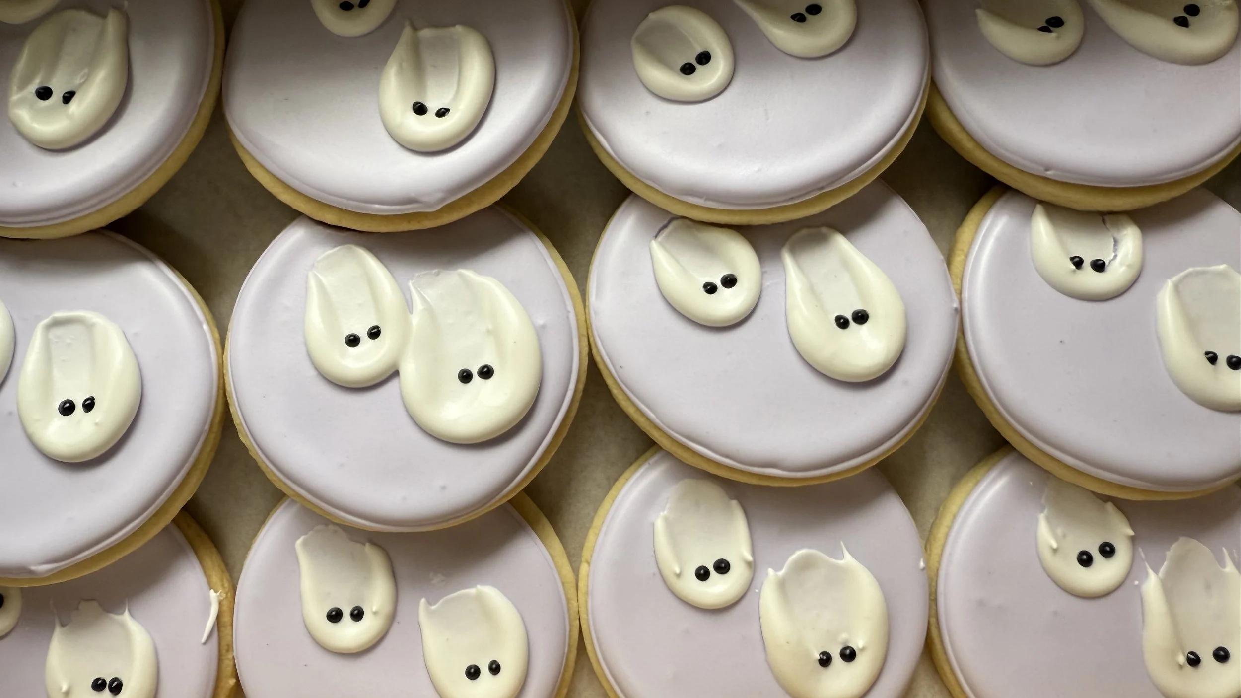 Group of ghost-themed sugar cookies decorated with white icing and black eyes, arranged on a surface.