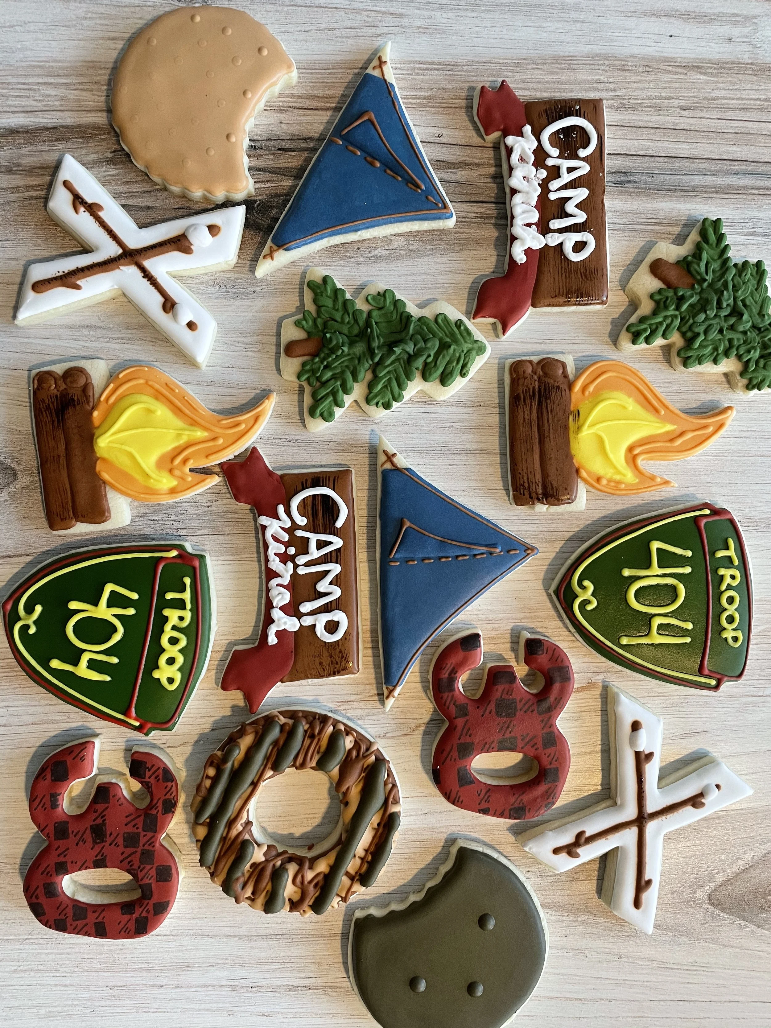 Assorted decorated cookies with Christmas theme, including a reindeer, Christmas trees, snowflake, candles, and a green gift box, all laid on a wooden surface.