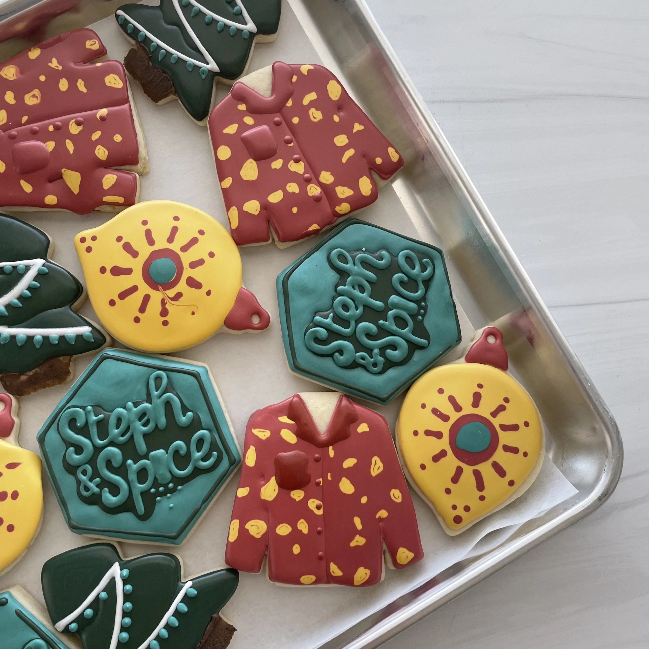 Decorated Christmas cookies shaped like Christmas trees, mittens, and holiday symbols, decorated with colorful icing and sprinkles, placed on a tray.