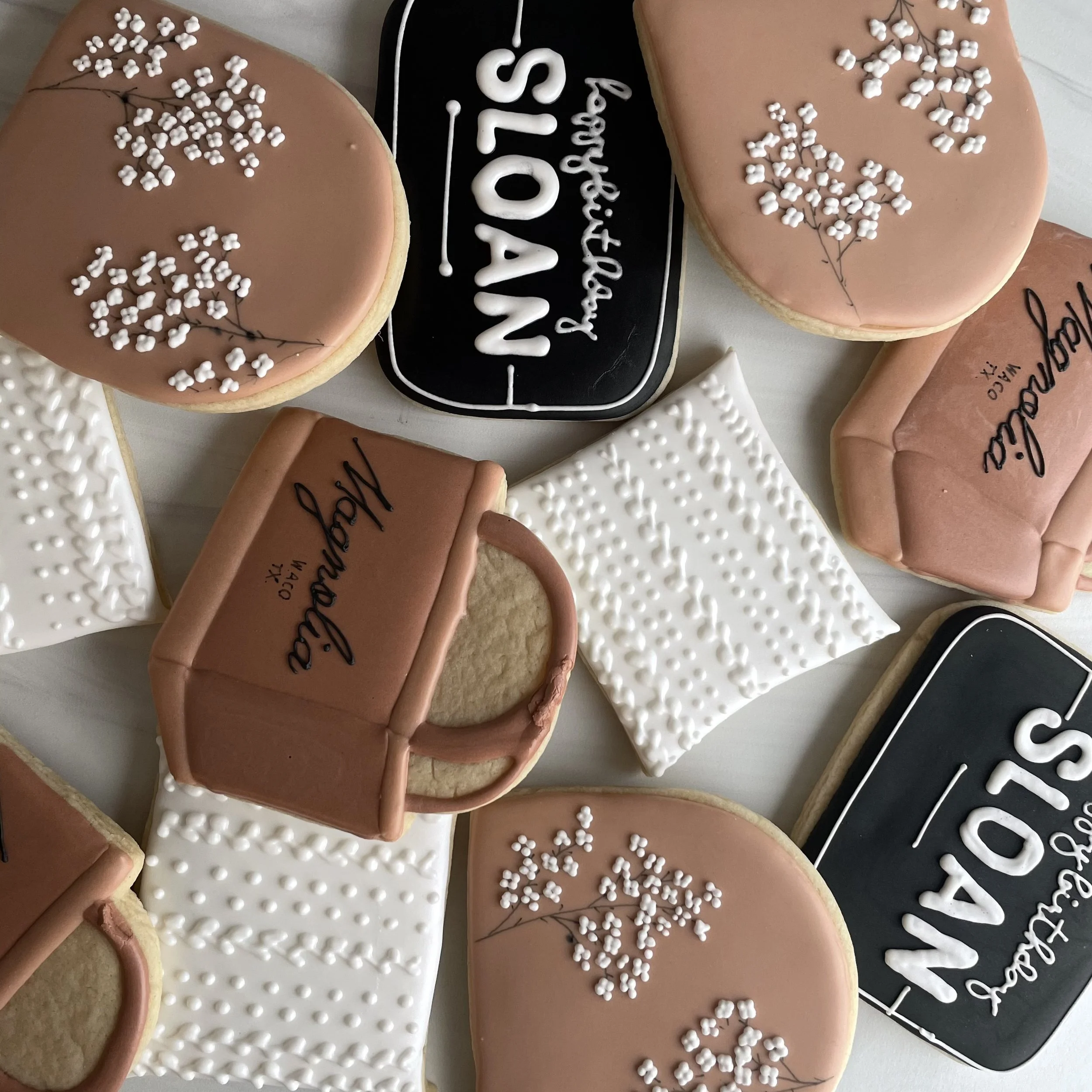 Assorted decorated cookies, some with white icing and floral patterns, and a rectangular black cookie with white icing that reads 'Happy Father'S Day'.