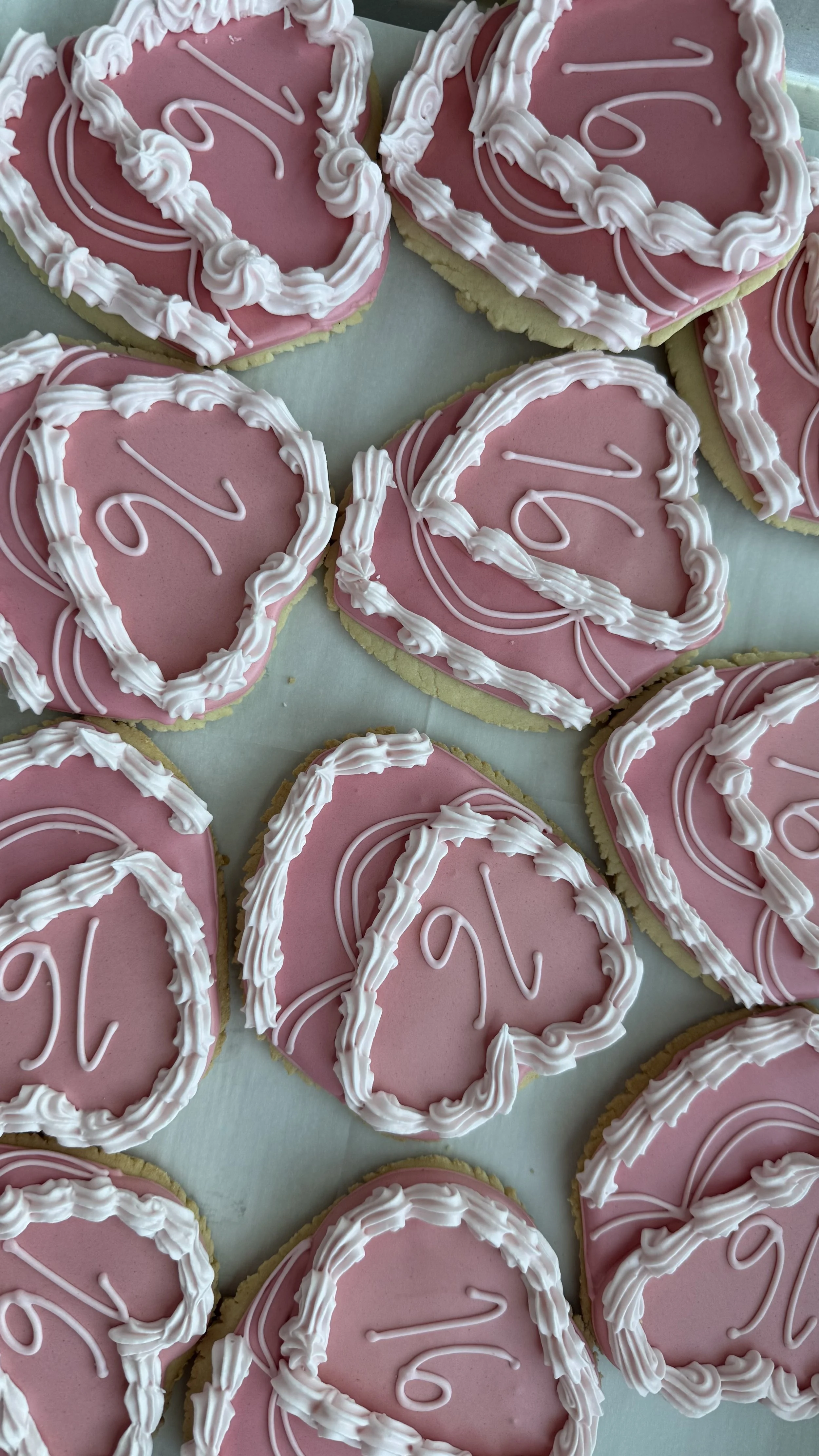 Heart-shaped cookies with pink icing, white piping border, and a white letter "S" in the center.