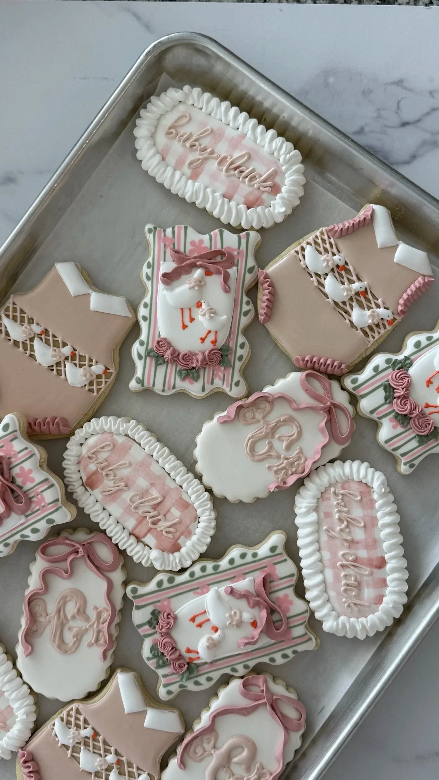 Assorted decorated cookies with pink and white icing, some featuring stork designs, ribbons, and the phrase 'baby clark' in cursive.