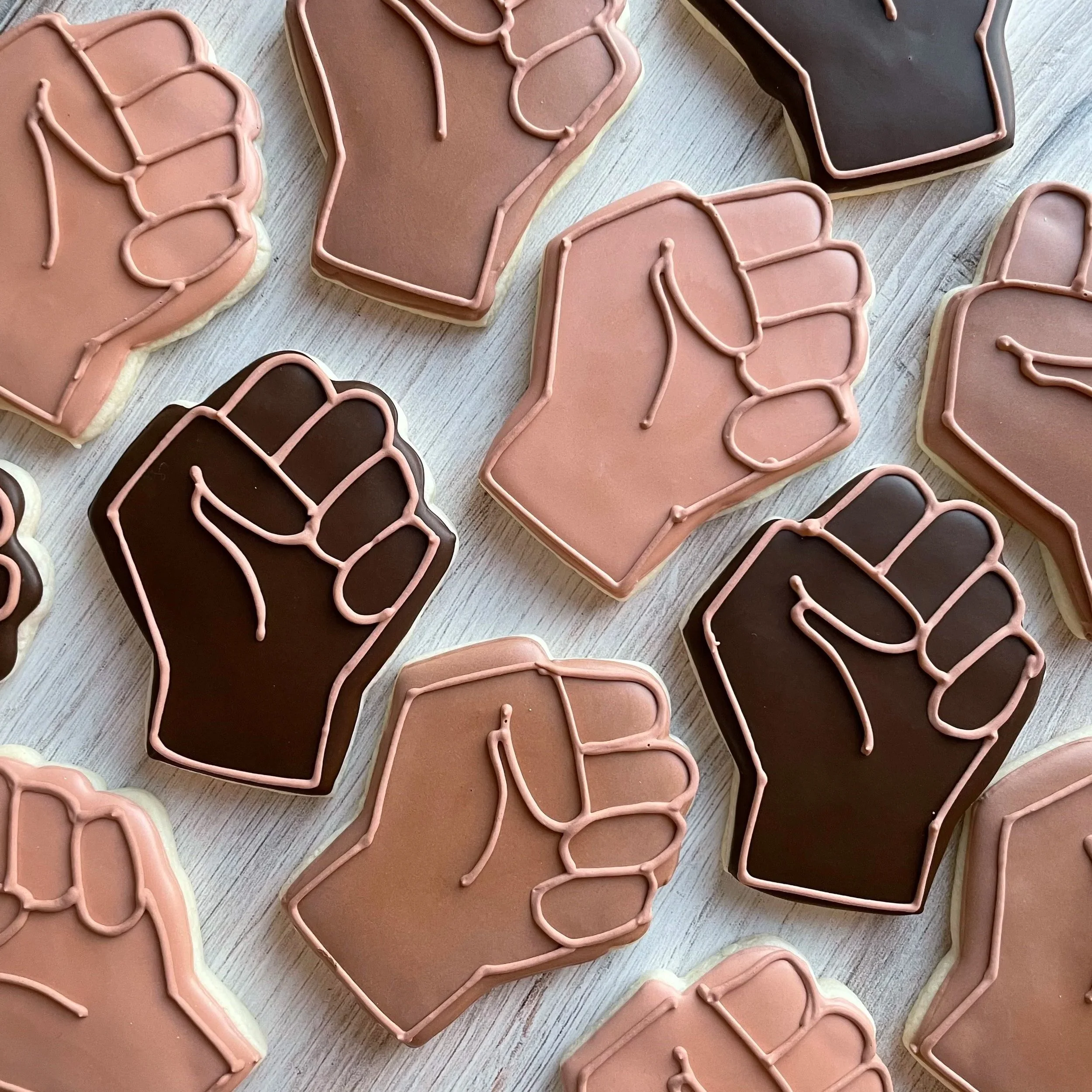Close-up view of decorated cookies shaped like animals with pink and dark brown icing and pink icing details, placed on a light-colored wooden surface.