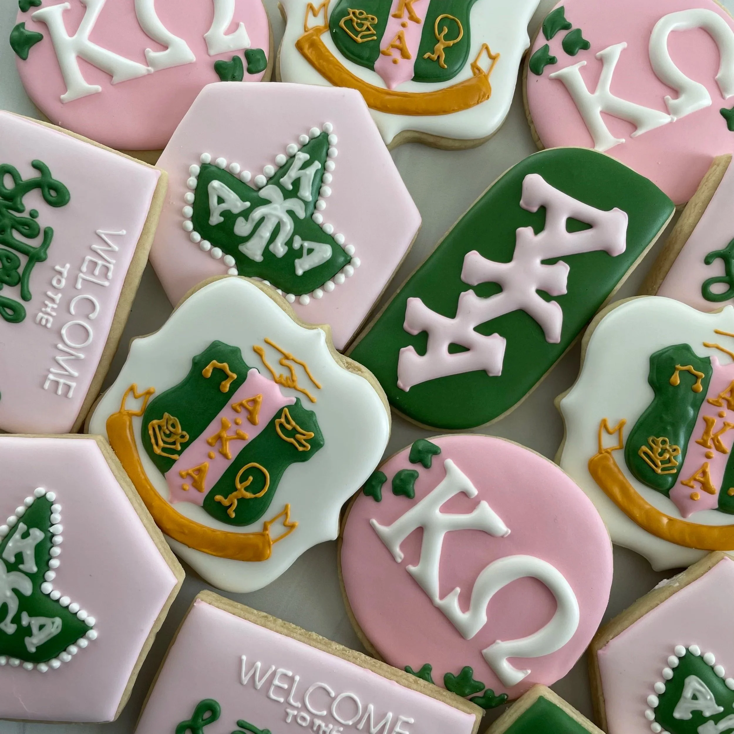 Decorated sugar cookies with pink, white, and green icing featuring holiday themes like Christmas trees, snowflakes, and the word 'Welcome.'