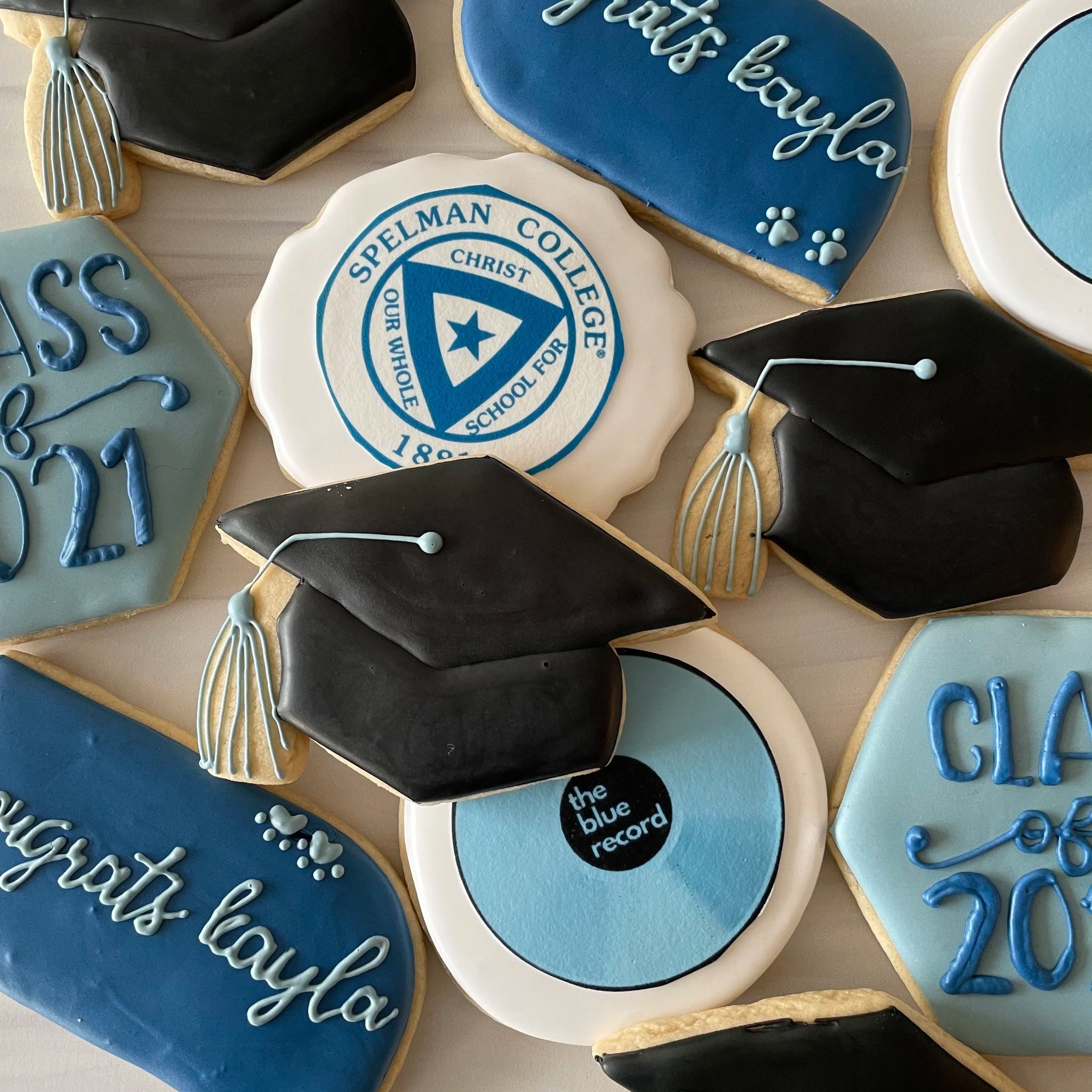 Decorated cookies with blue, white, and black icing, featuring college logos, text, and educational themes.