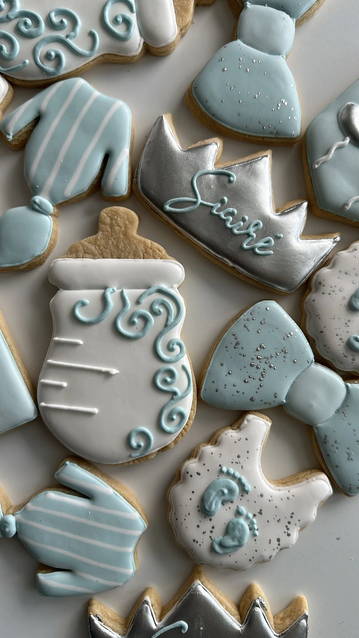 Decorated cookies with baby shower theme, featuring blue, white, and silver icing designs of bottles, stars, and the word 'Baby'.