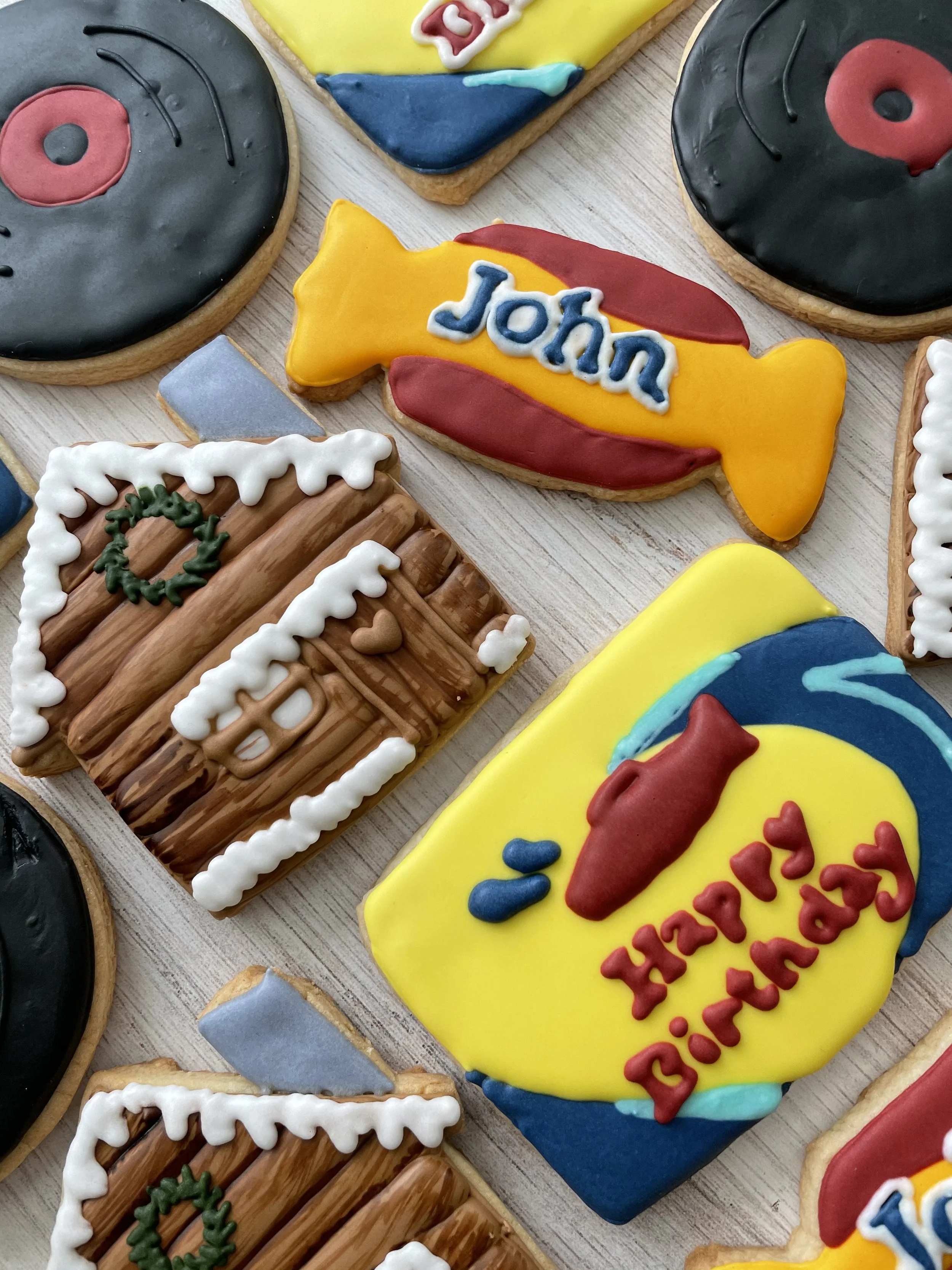 Decorated cookies with holiday and greeting themes, including one with the name 'John' and another with a restaurant logo design.