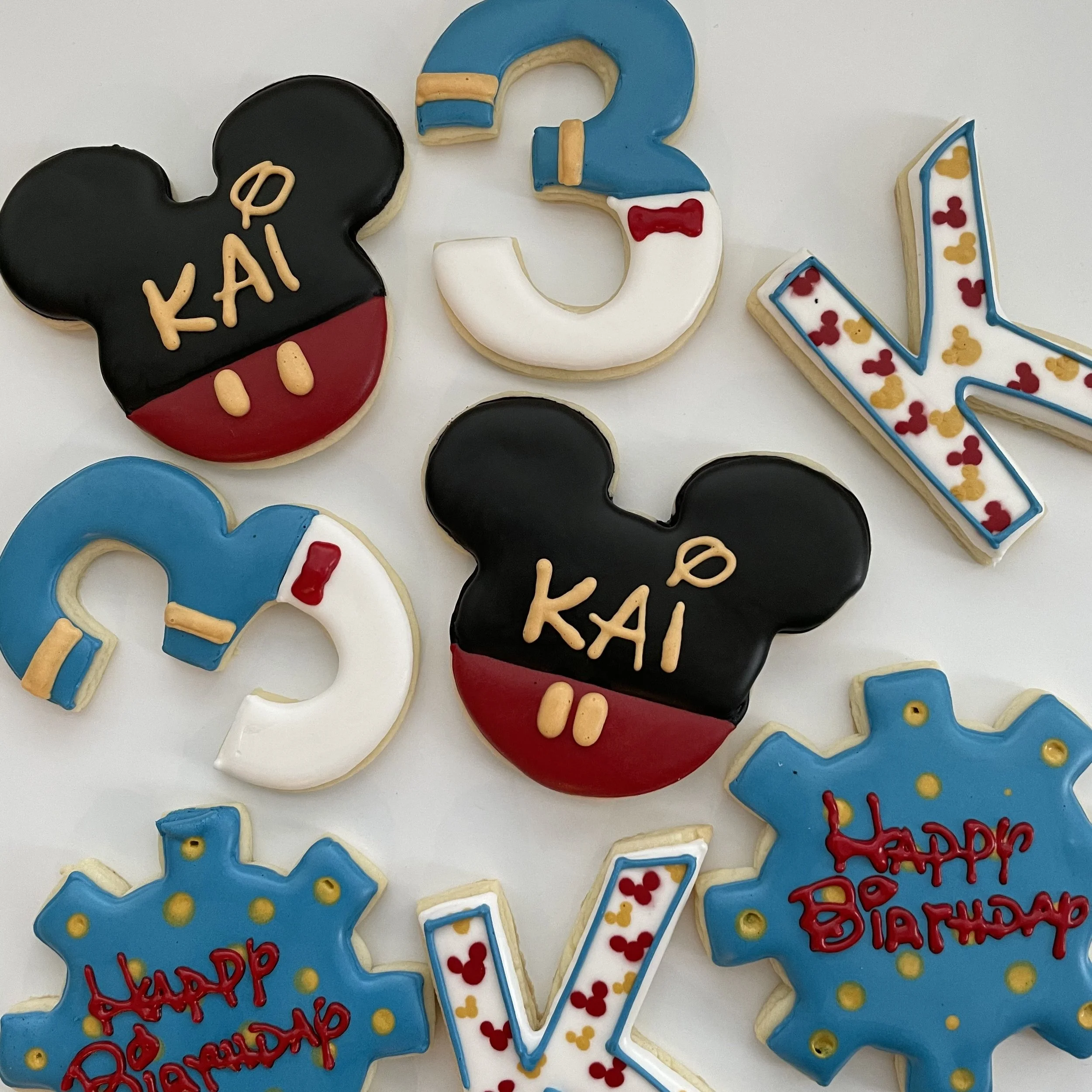 Colorful birthday cookies decorated with various themes including Mickey Mouse ears, the number 3, and the number 1 with birthday message and confetti.