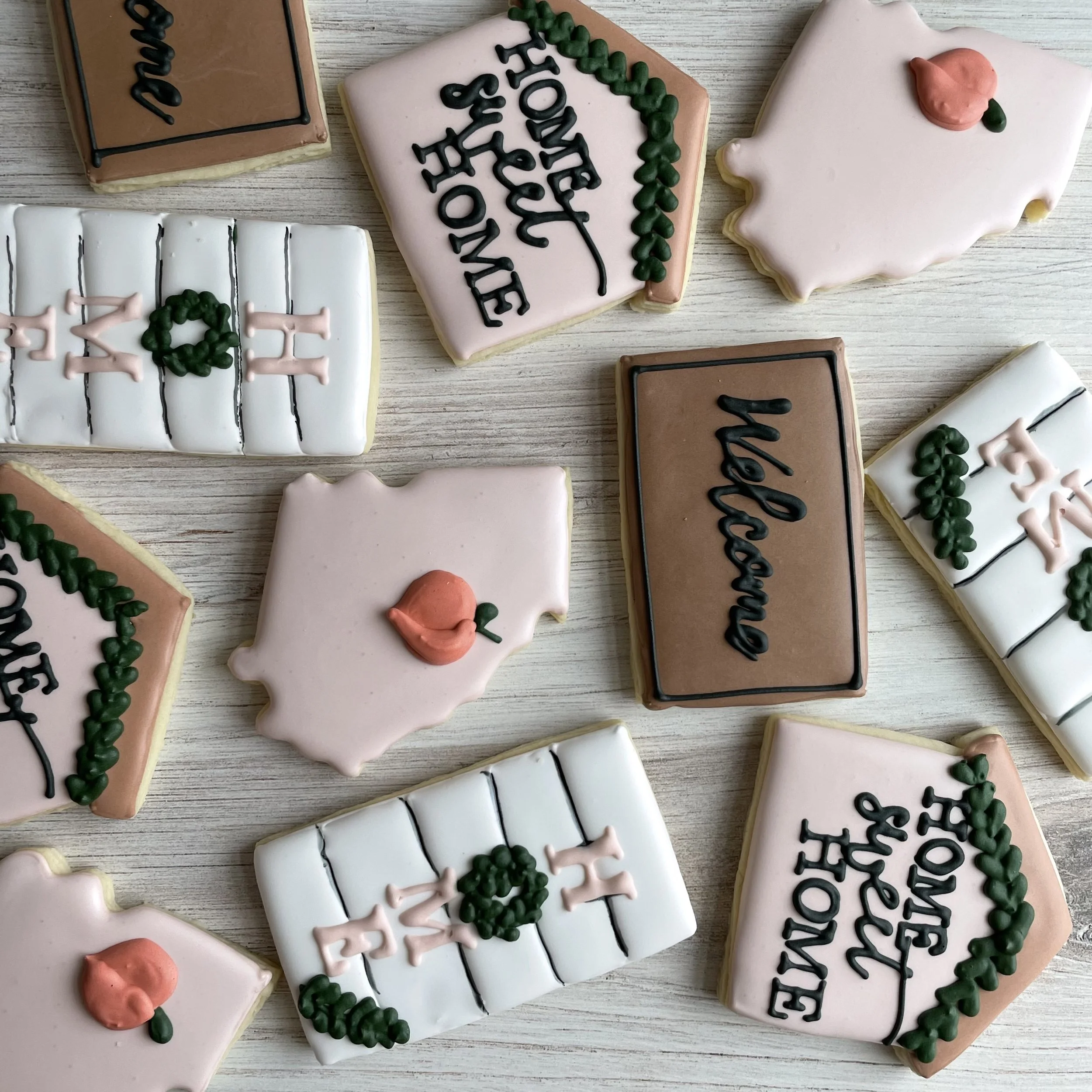 Assorted decorated cookies on a wooden surface, featuring messages and designs. One cookie reads 'Best' with a green wreath, another says 'Valentine' with black icing, and others have decorative patterns.