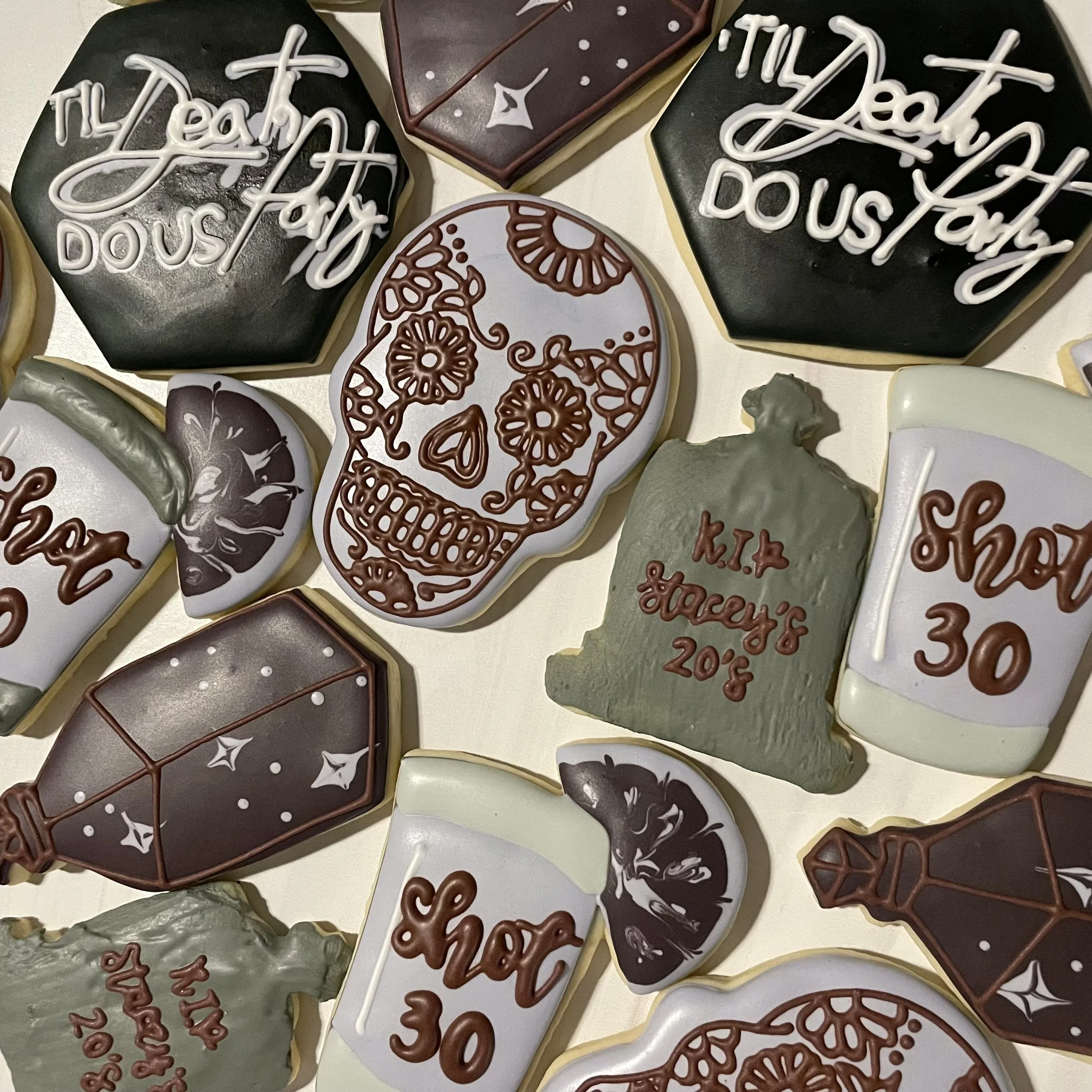 Assorted decorated cookies with Halloween and fall-themed designs, some with messages like 'Happy Halloween' and 'Treats', featuring skull, floral, and geometric patterns, on a white surface.