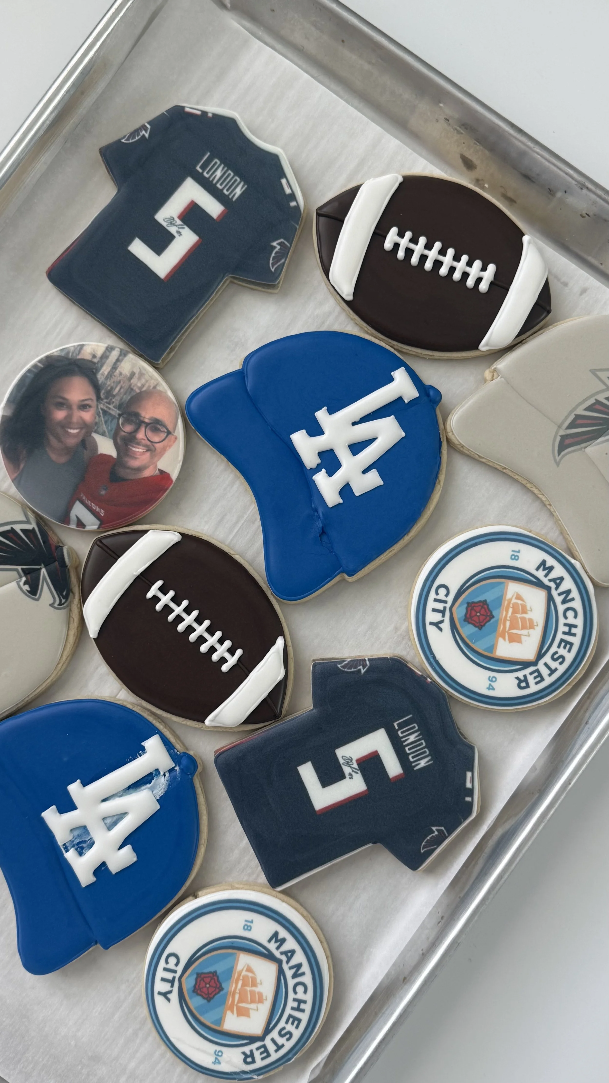 Decorated sugar cookies with football and sports team themes, including cookies shaped like footballs and team logos, on a silver tray.