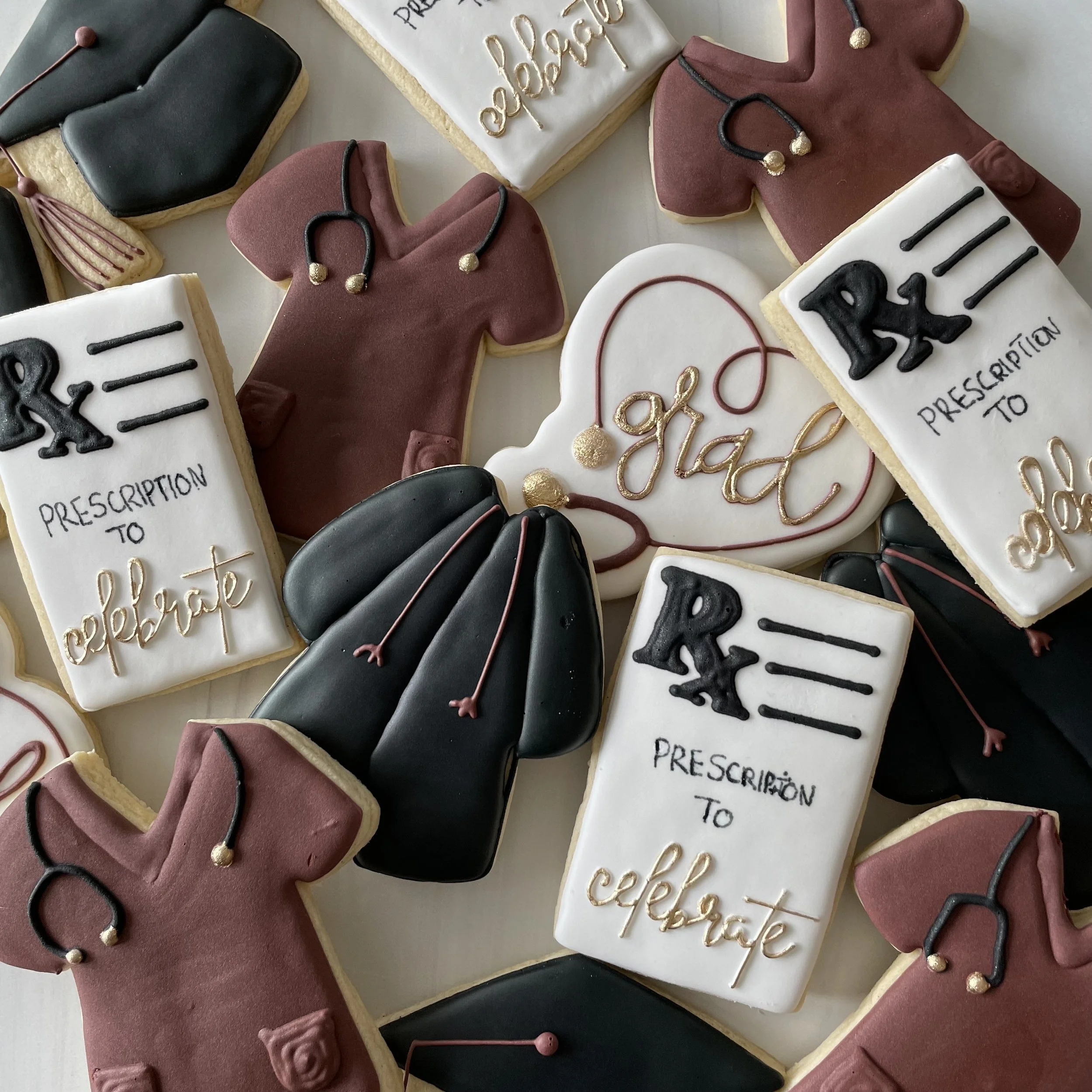 Decorated sugar cookies with medical school themes, including stethoscopes, test tubes, and graduation caps, some with patriotic red, white, and blue colors, and one cookie with the phrase 'PRESCRIPTION TO PERFECT' written on it.