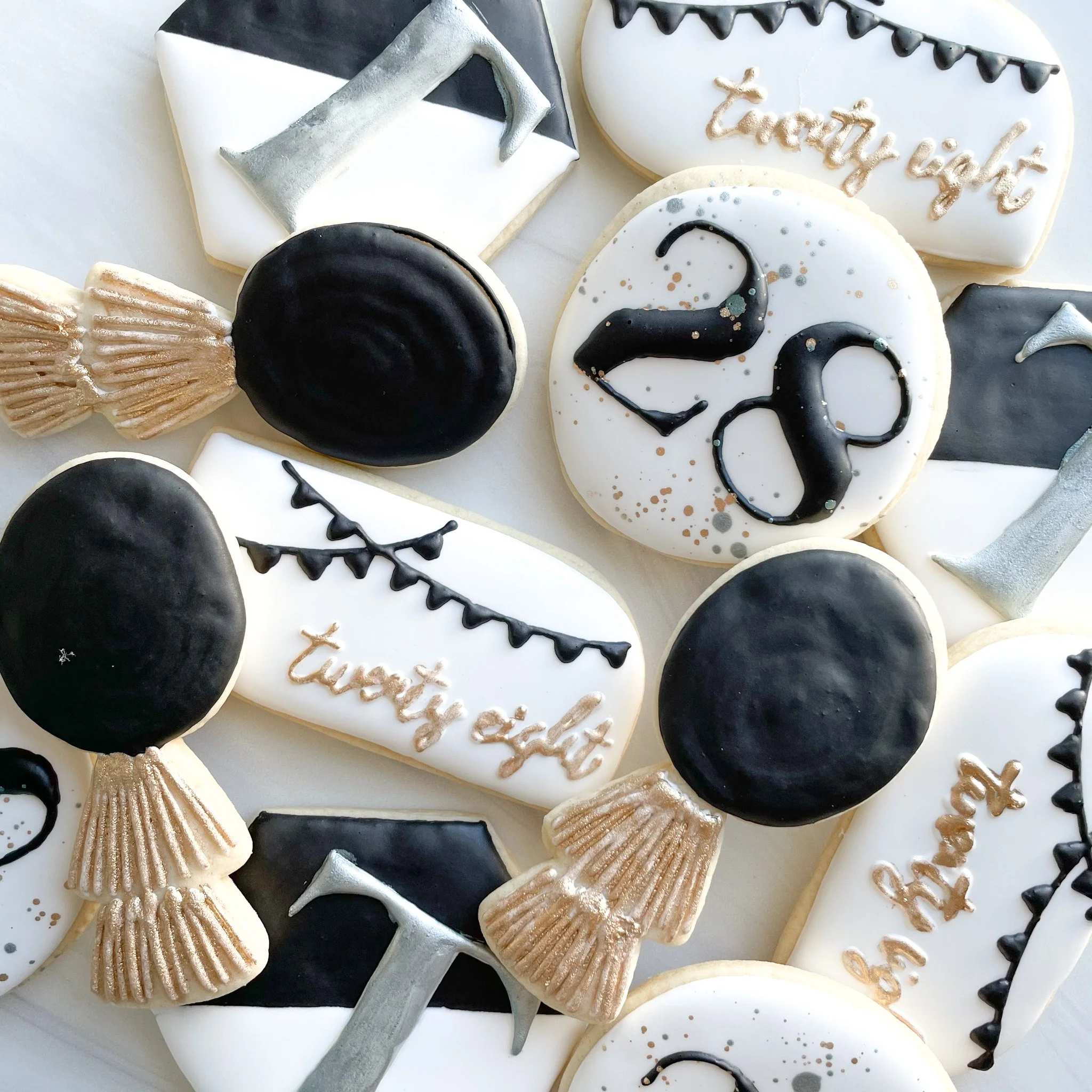 Assorted decorated cookies with Halloween and Thanksgiving themes, including black and white colors, with messages such as 'happy' and 'thankful' written in icing, some shaped like pumpkins and spanning various designs.