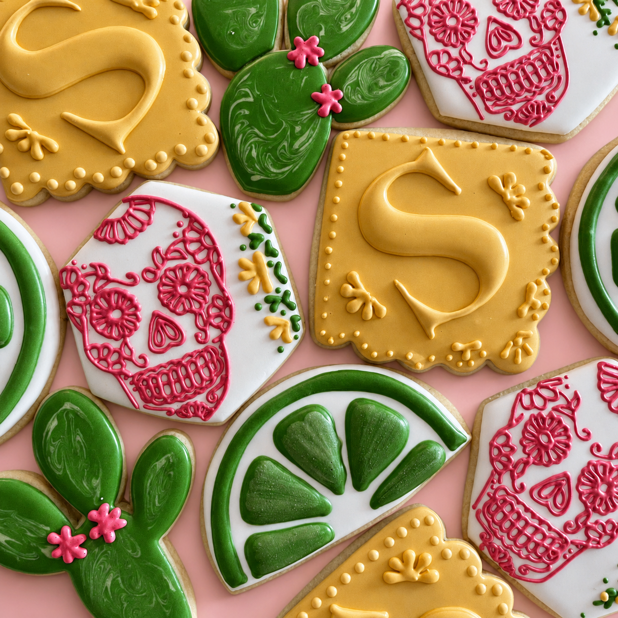 Colorful decorated sugar cookies with Frida Kahlo and Day of the Dead themes, featuring skull and floral designs, on a pink background.