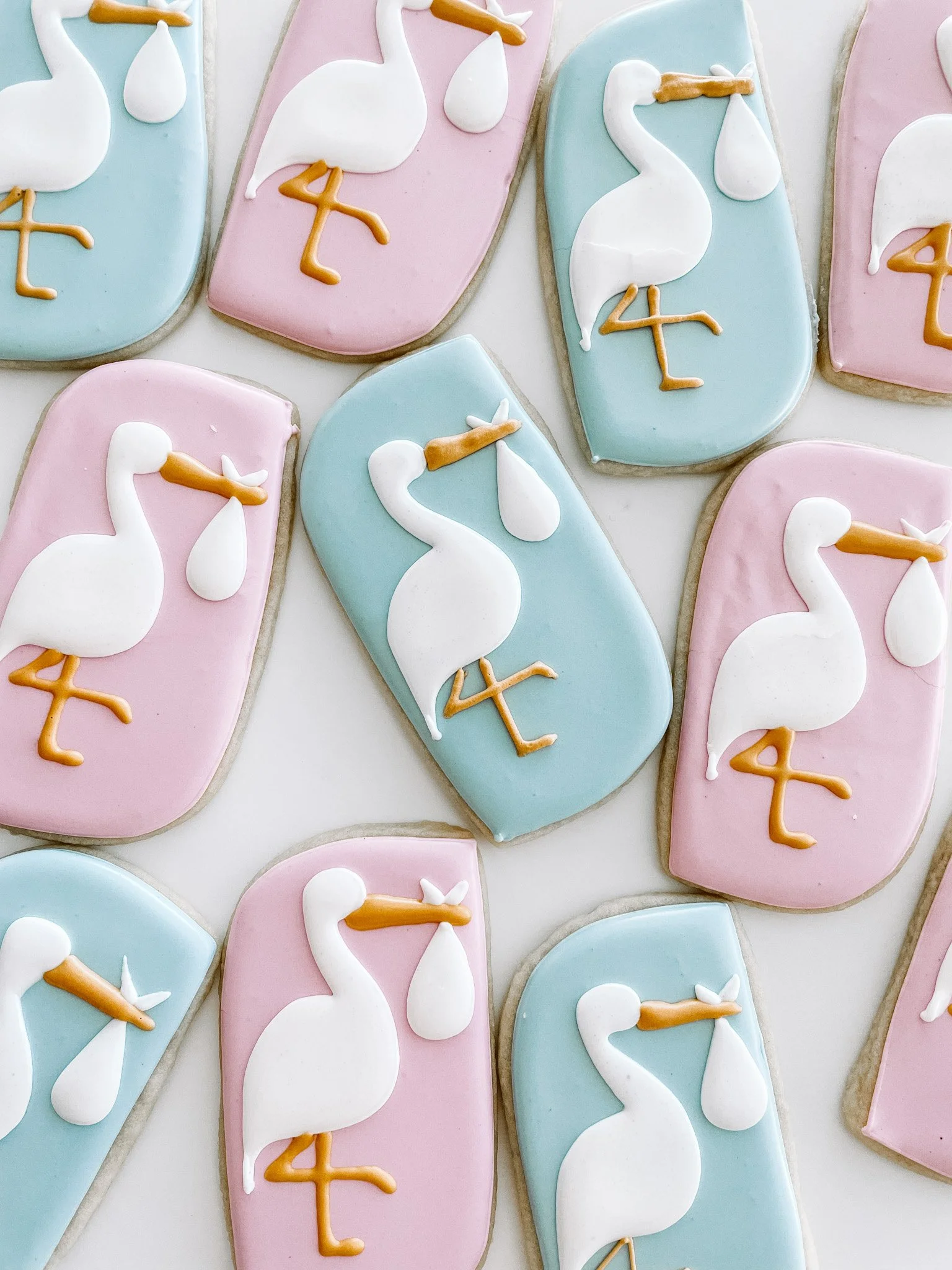 Decorated cookies with pastel pink and blue icing featuring white swan designs and the number 4 in orange icing.