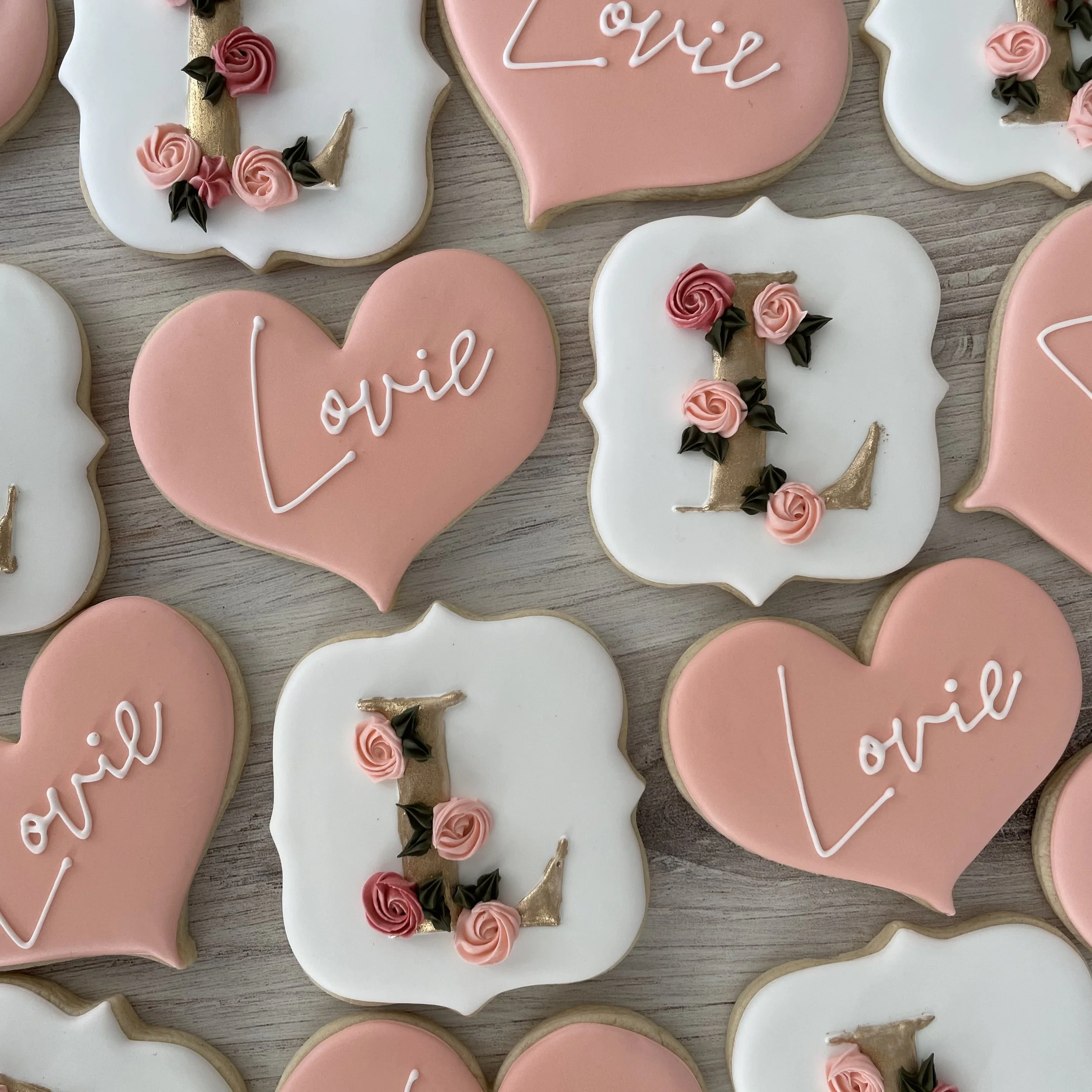 Assorted decorated sugar cookies in pink and white with floral and unicorn motifs, some with the words 'love' and 'joy' written on them.