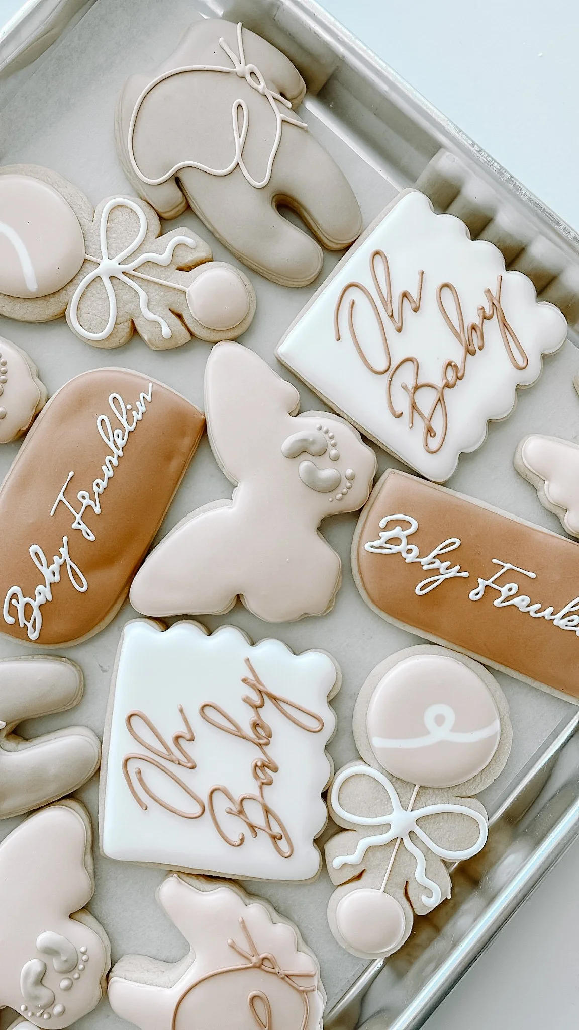 Assorted cookies with beige, white, and pink icing, decorated with words like "Baby Trump" and "Thank you" along with bows, hearts, and other designs.