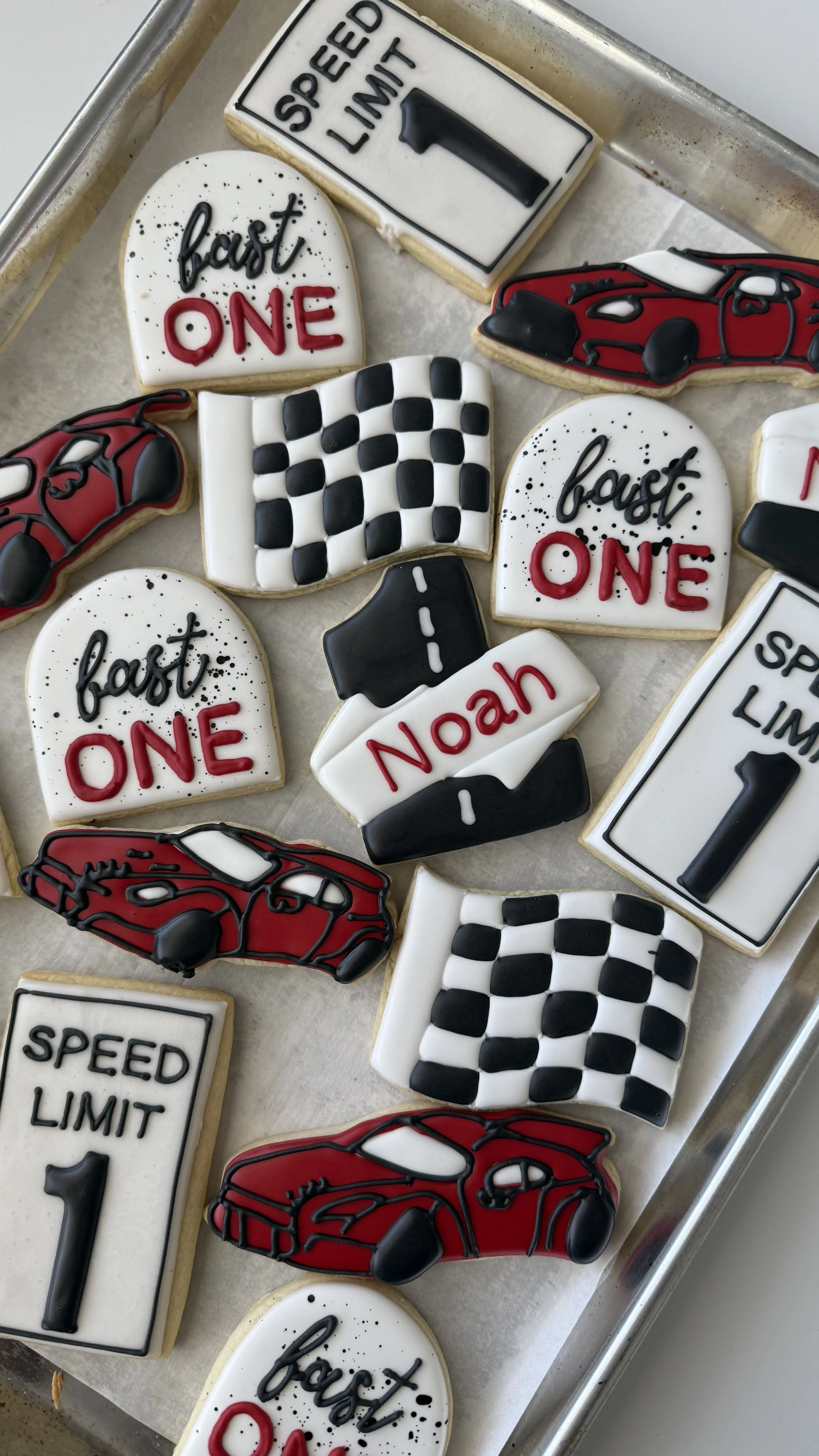 Cookies decorated with racing car themes, checkered flags, speed limit signs, and text like "fast ONE."