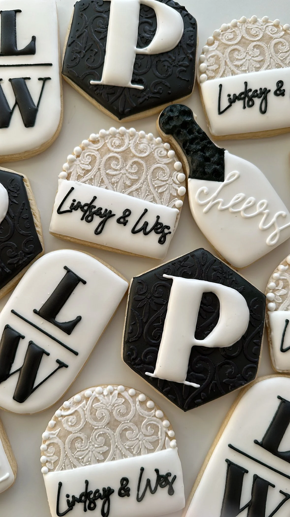 Decorated cookies in black, white, and beige with various patterns and text such as 'Lindsey & Wex' and 'Cheers'.