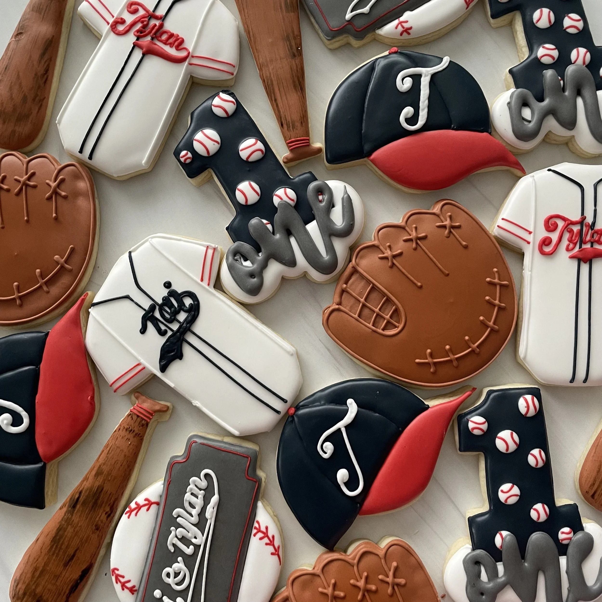 Assorted baseball-themed decorated cookies on a wooden surface, featuring baseballs, bats, gloves, hats, and team names in red, black, white, and gray icing.