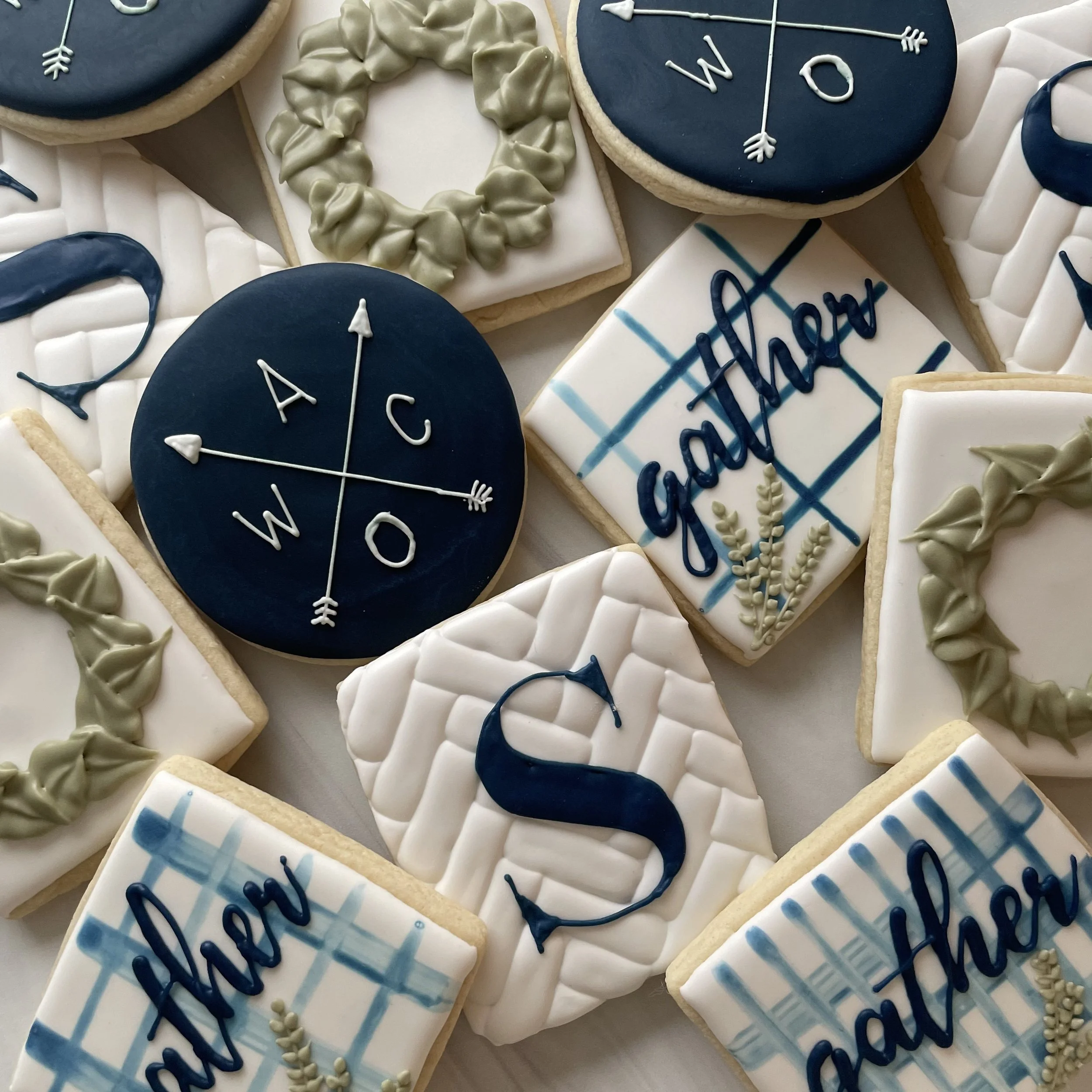 Decorated cookies with nautical theme, featuring navy blue, white, and beige colors, with compass, arrow, and writing motifs.