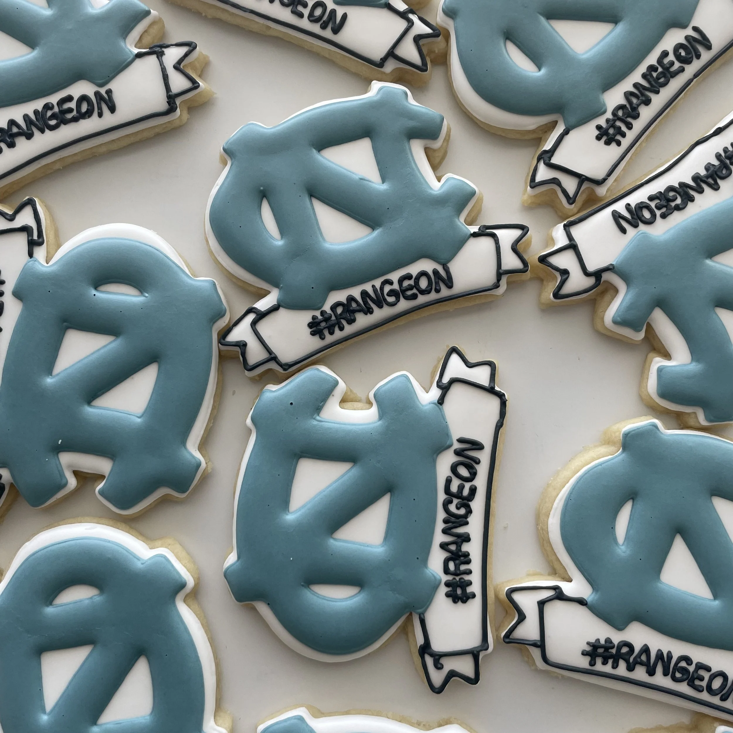 Close-up of decorated cookies shaped like shark fins with light blue icing and black outlines, along with white icing cookies with black text and hashtag hashtag #TRANGEN.