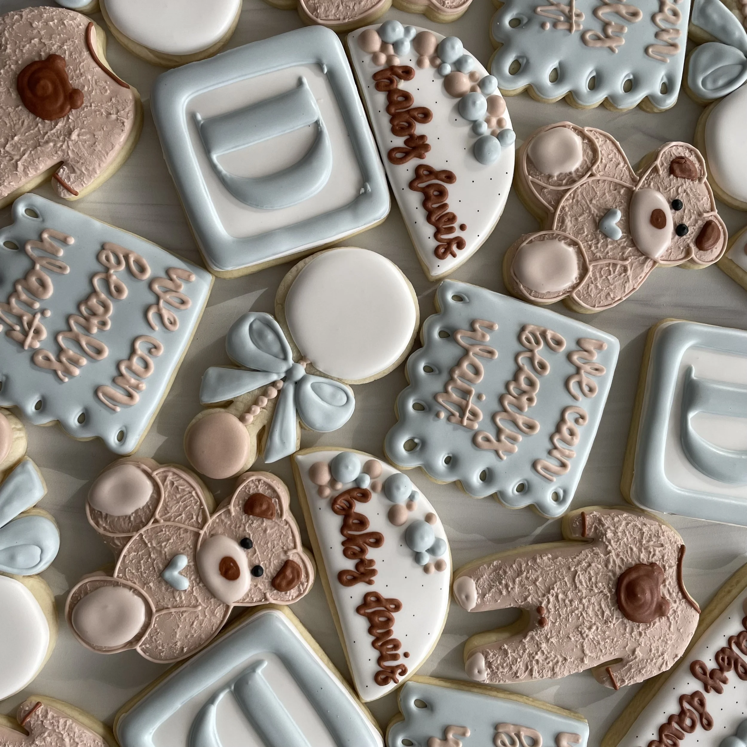 Assorted decorated cookies with pastel colors, featuring message like "Happy Birthday" and a teddy bear shape.