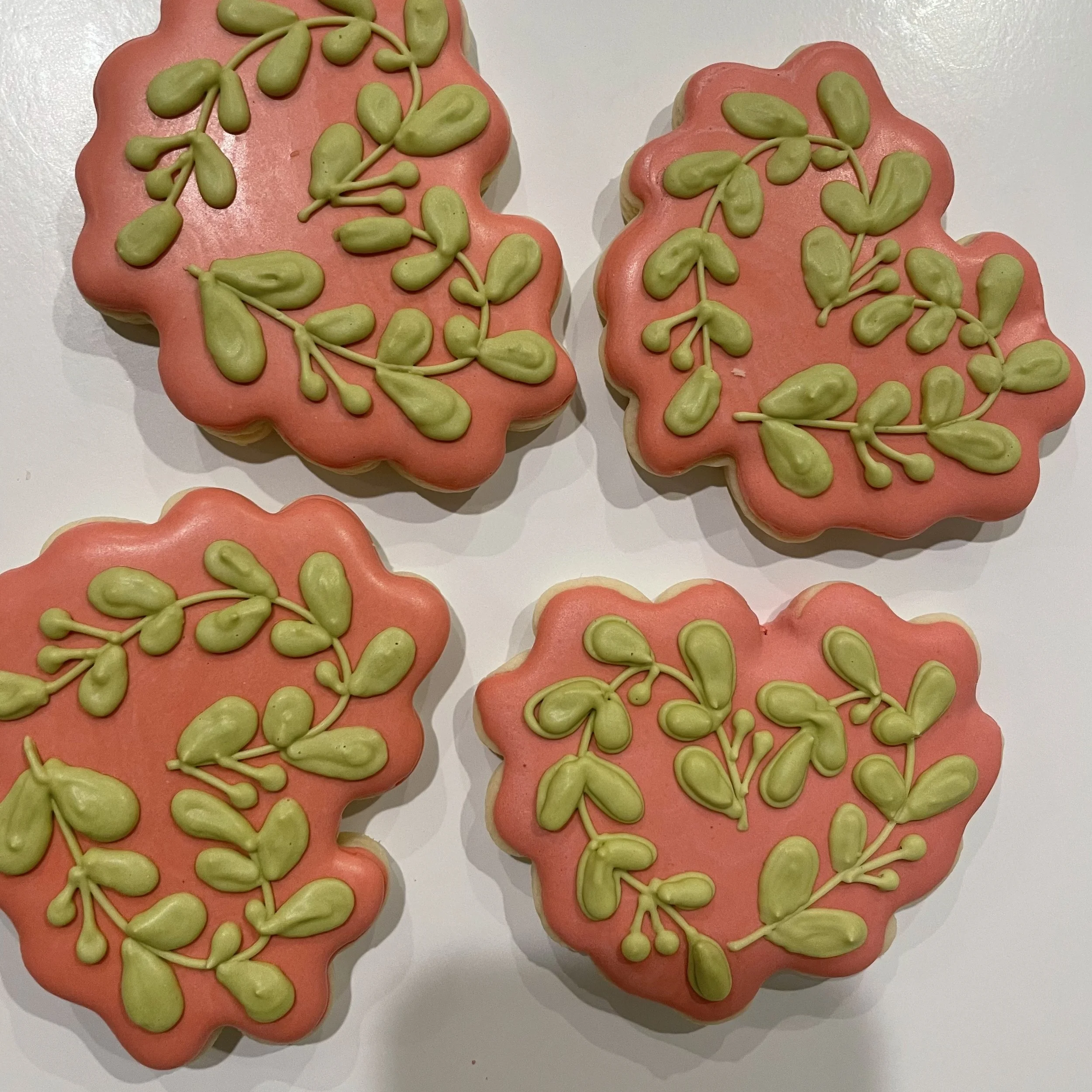 Decorated cookies with pink and green icing, shaped like leaves and branches.