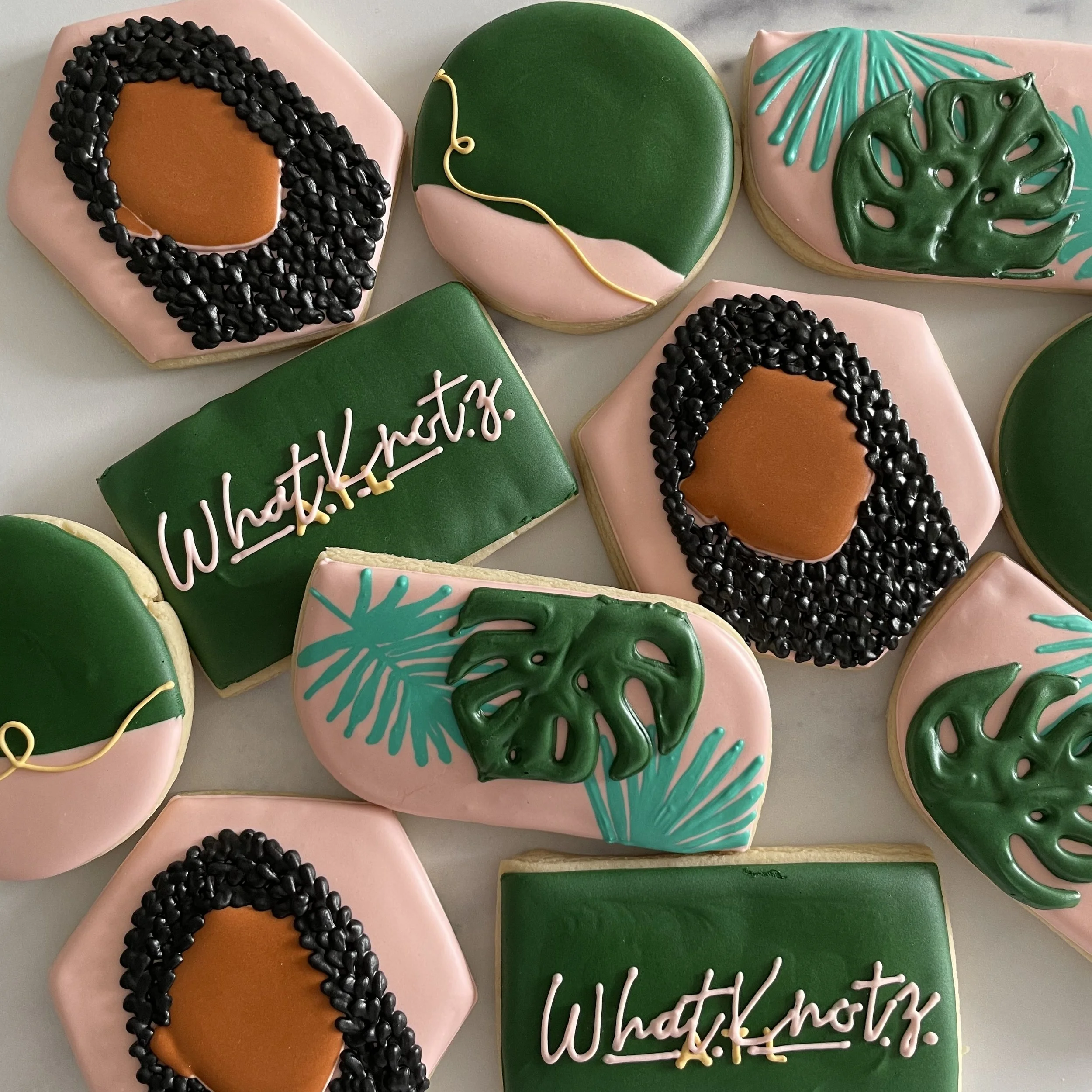 Decorated cookies with various designs, including tropical leaves, abstract patterns, and congratulatory messages, decorated with colorful icing.