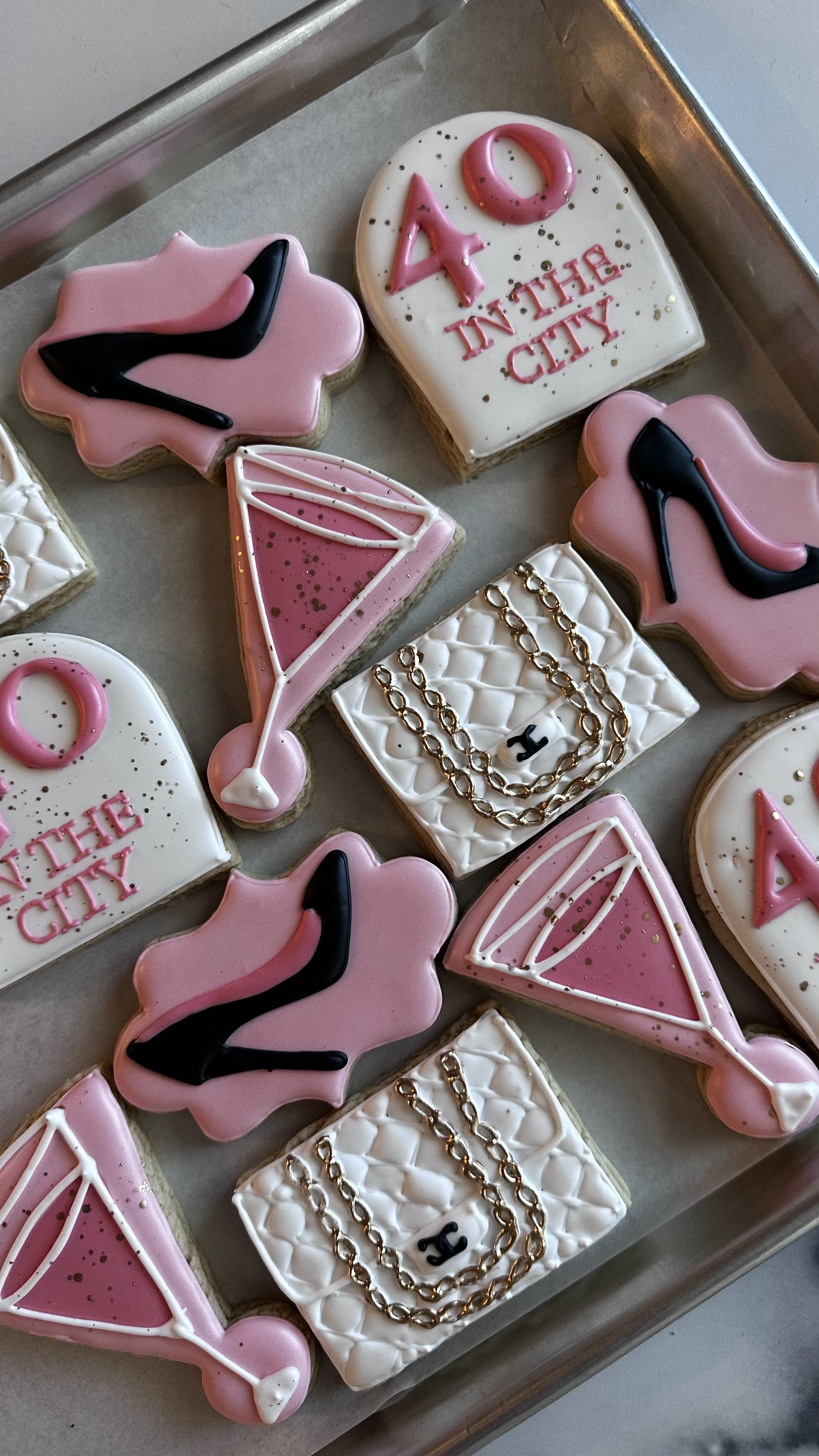 Decorated cookies with themes of fashion, jewelry, and New York City, including high heels, a diamond, and chains, on a baking tray.