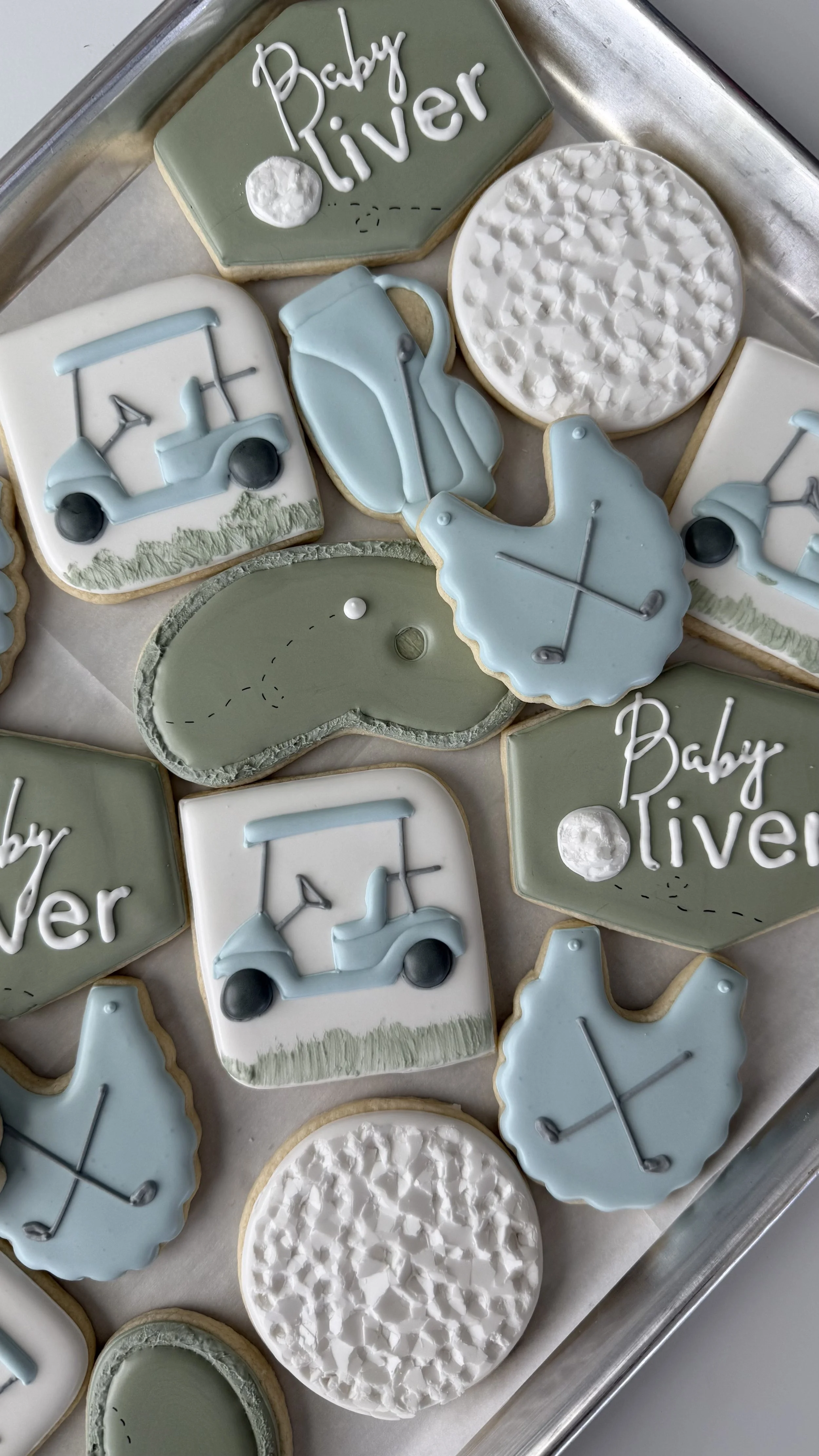 Decorated cookies with a golf theme and baby shower message, featuring golf carts, golf balls, and the words "Baby Oliver" on some cookies.