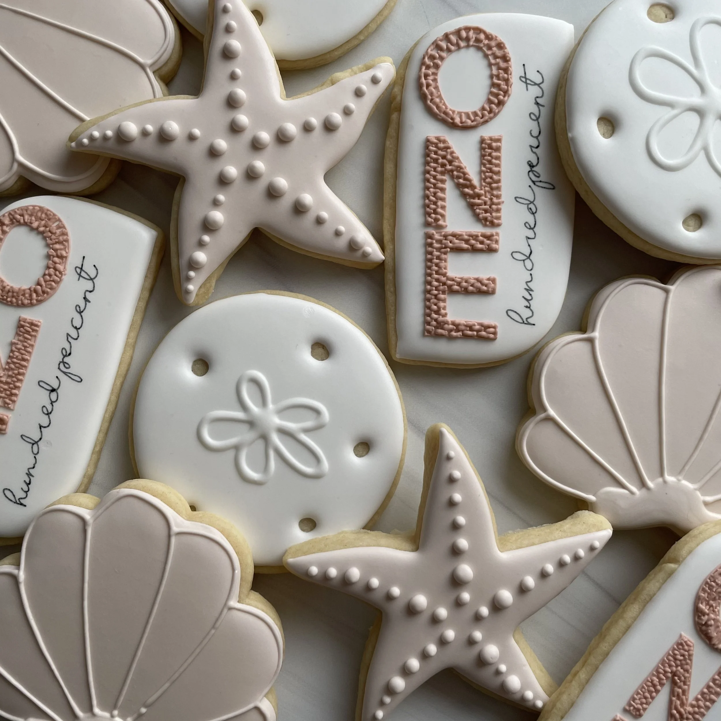 Decorated cookies with white and pink icing, some with the word 'LOVE' and decorative patterns, arranged on a flat surface.
