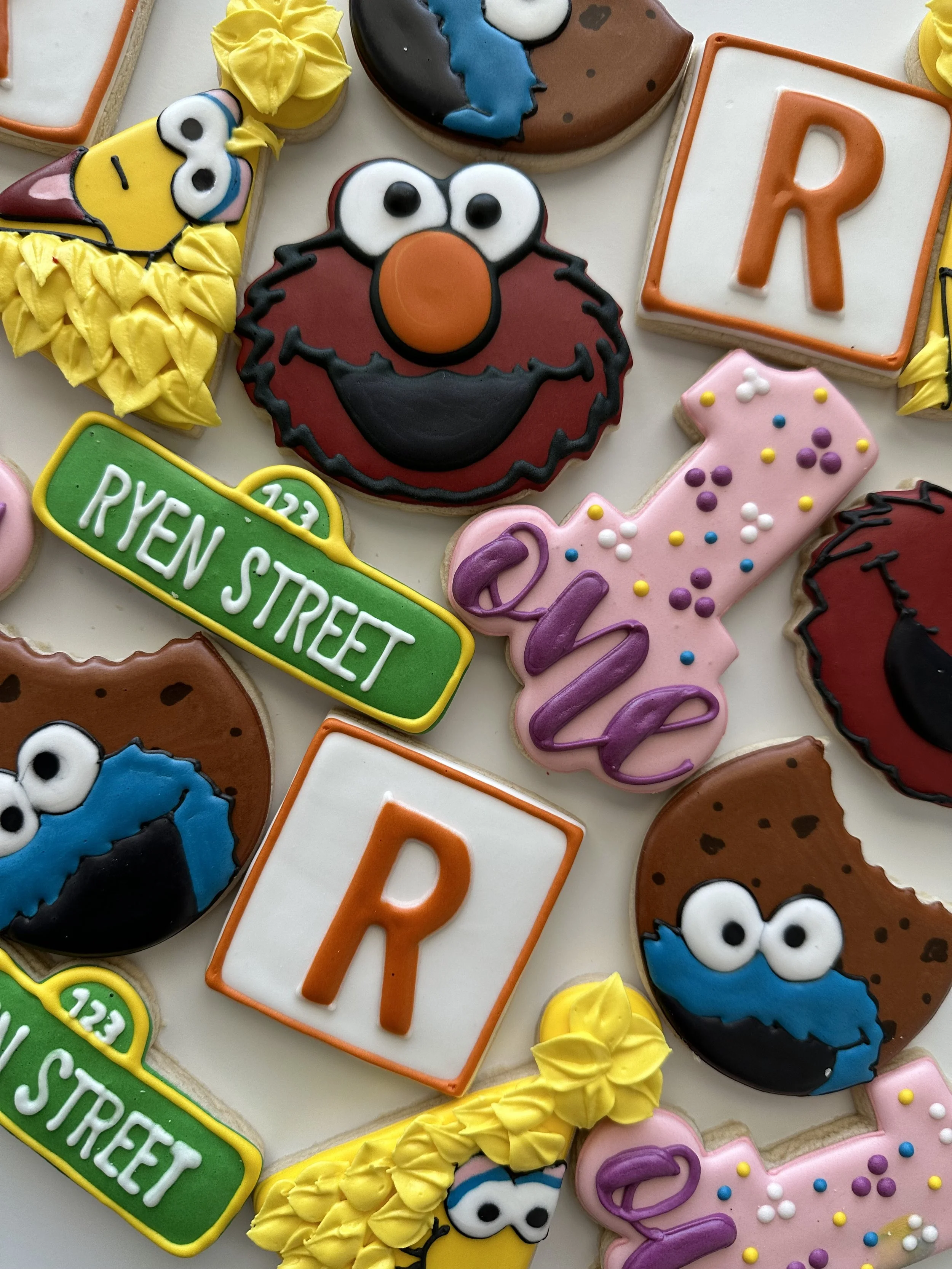 Decorated cookies featuring Sesame Street characters, including Cookie Monster, Elmo, Big Bird, and a sign reading 'Ritten Street', with colorful icing and sprinkles.