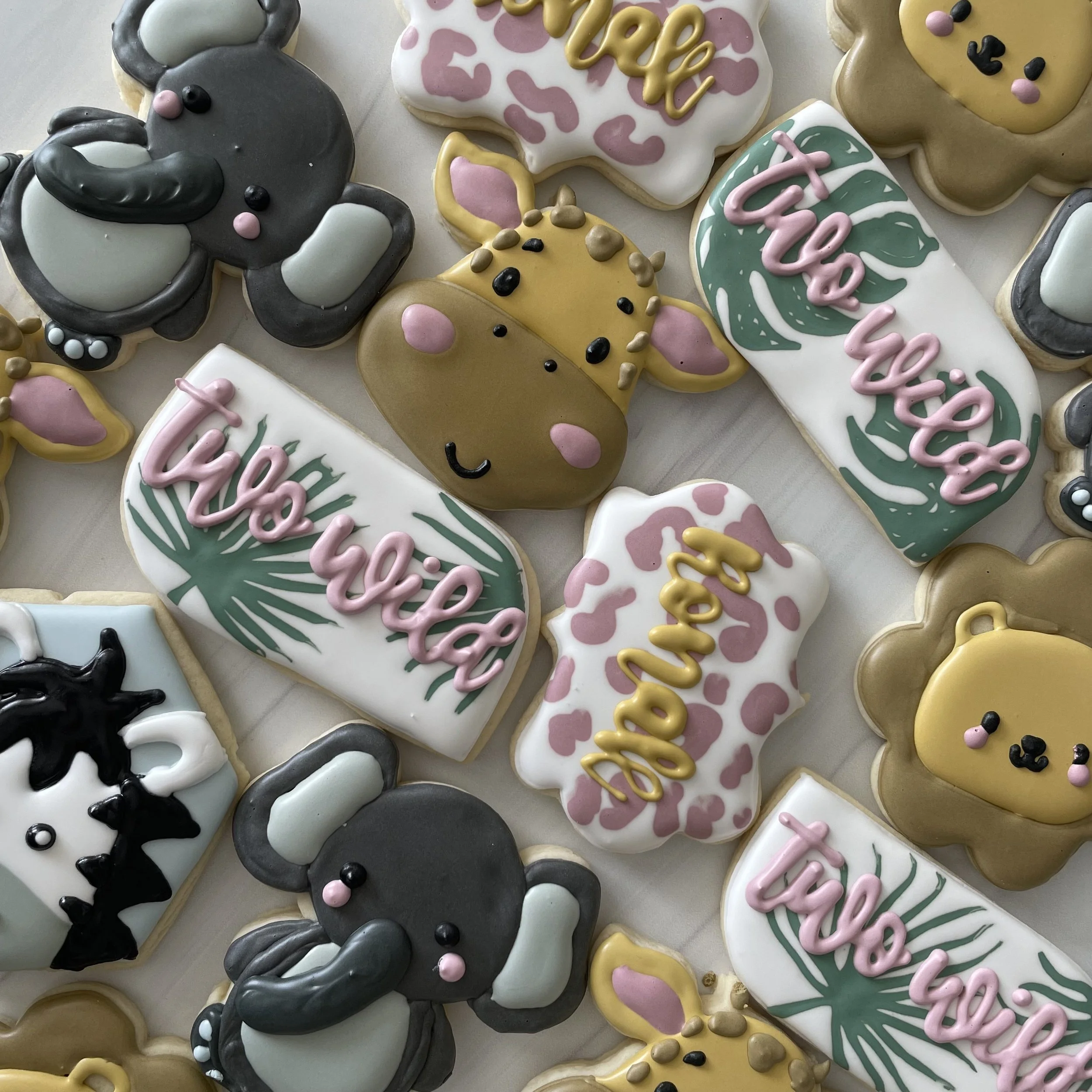 Assorted decorated cookies, including a gray bunny with pink and black facial features, a white cookie with pink spots and yellow writing, a yellow bunny with pink cheeks and black facial features, and a white cookie with green leaves and pink letter