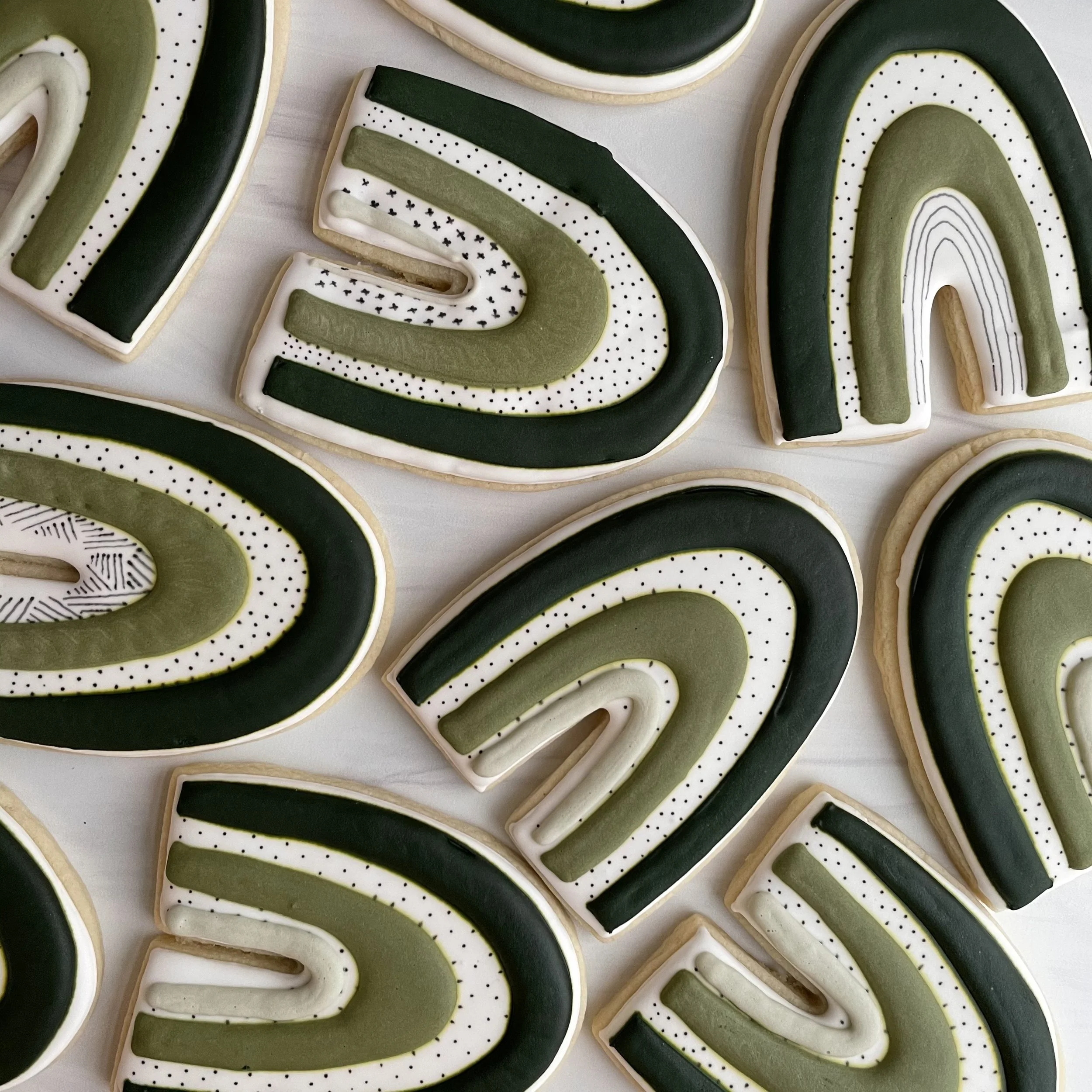 Close-up of decorated cookies with black, white, and olive green icing, featuring striped and dotted patterns.
