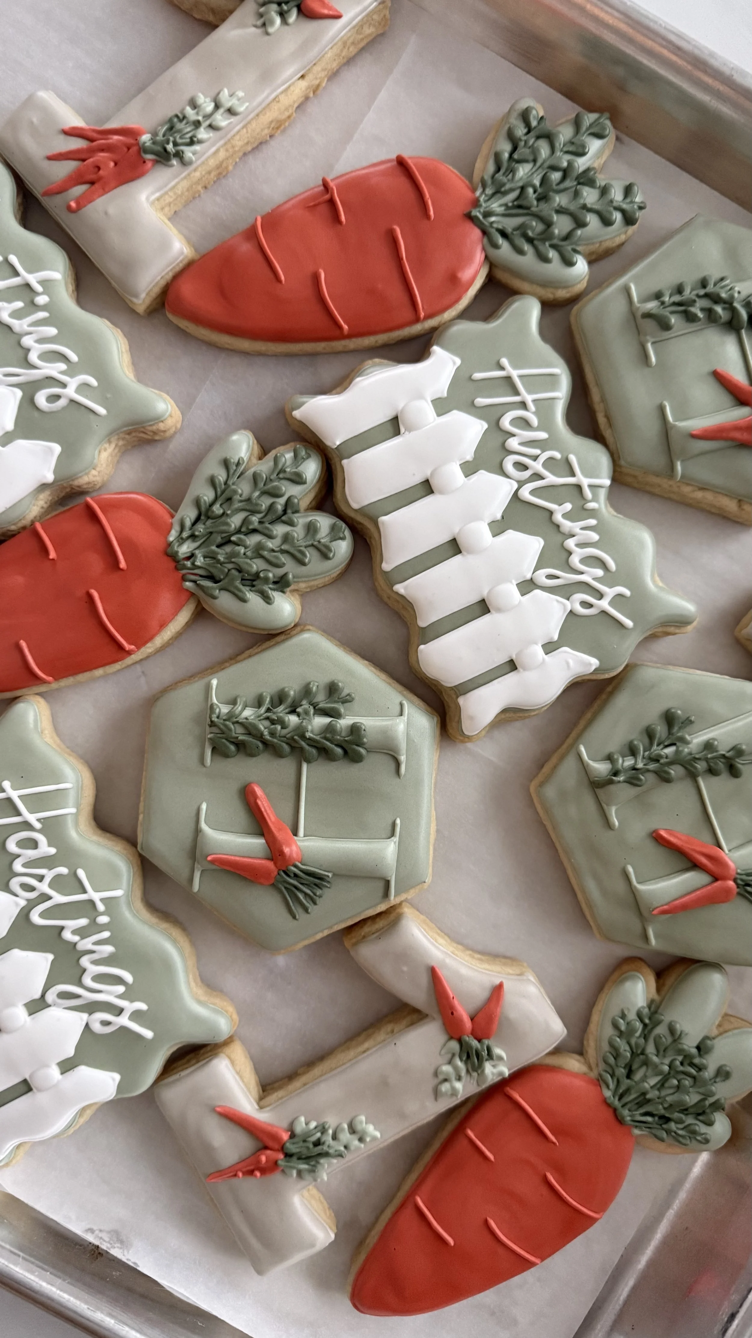 Holiday-themed decorated cookies shaped like carrots, holly leaves, Christmas trees, and Christmas trees with the phrase 'Happy Holidays' written on green cookies.