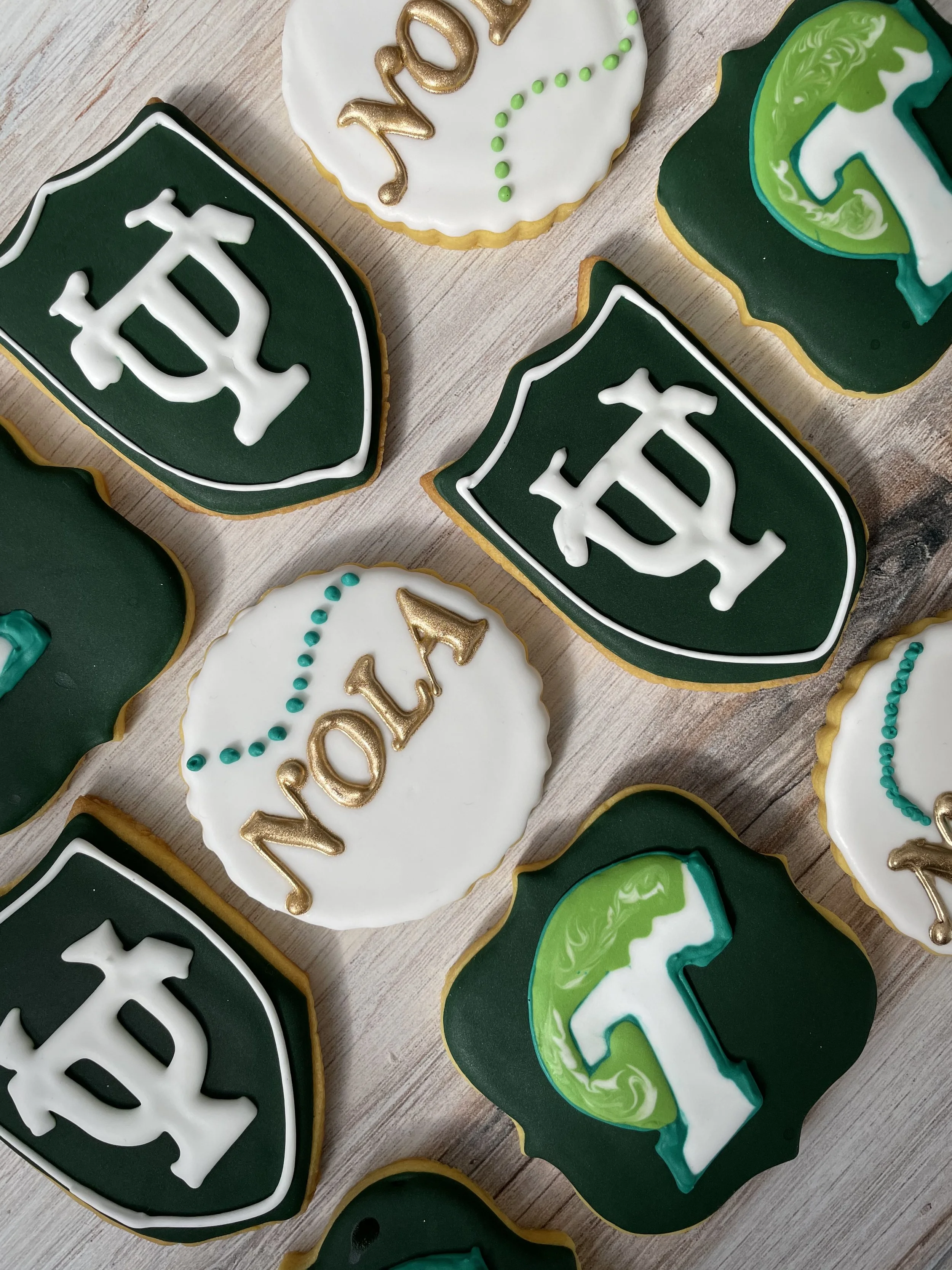 Decorated cookies with football-themed icing, featuring white, green, and gold accents, some with the word 'TOY' spelled out in icing.