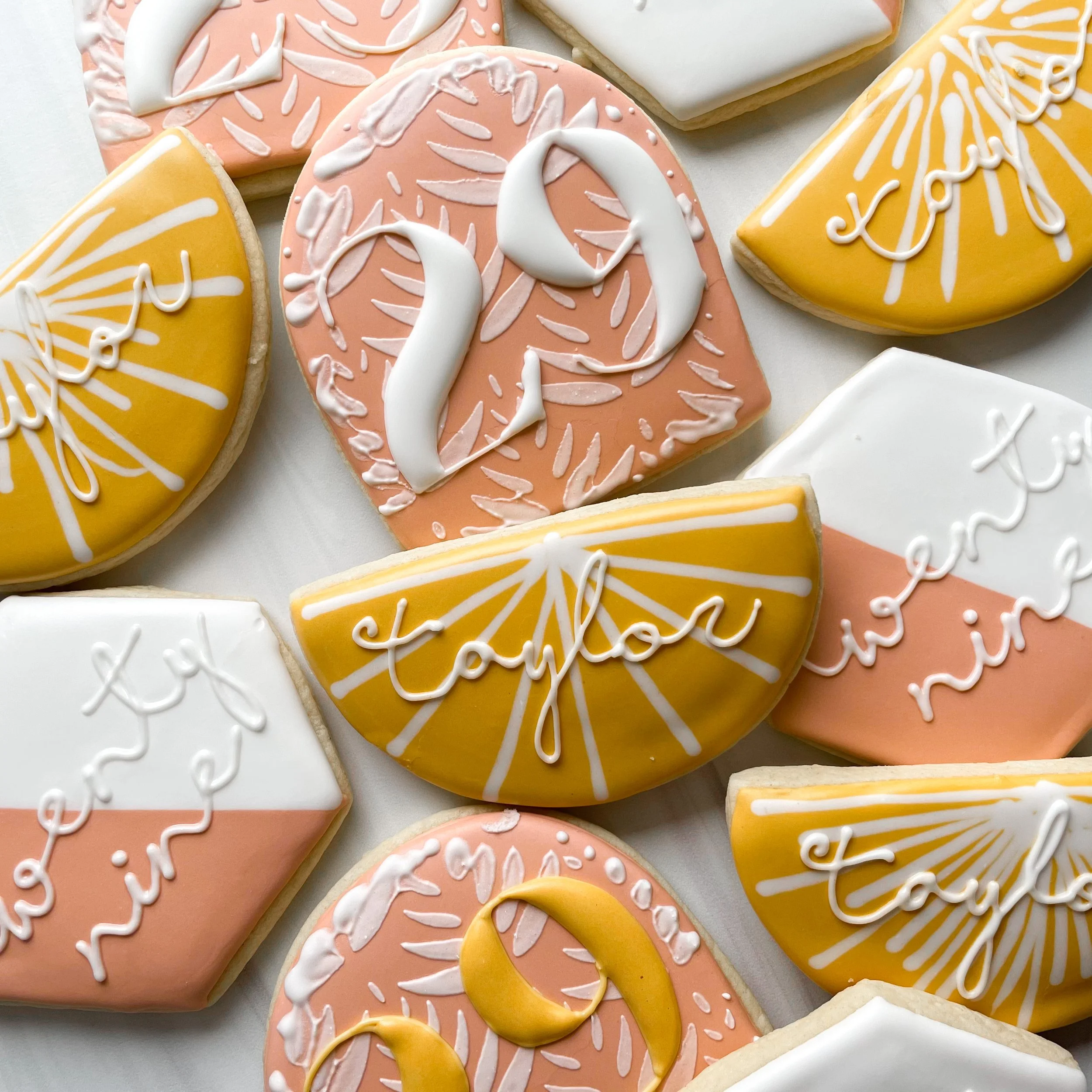 Decorated cookies with pastel colors, including pink, yellow, and white, featuring floral and calligraphy designs with white icing.