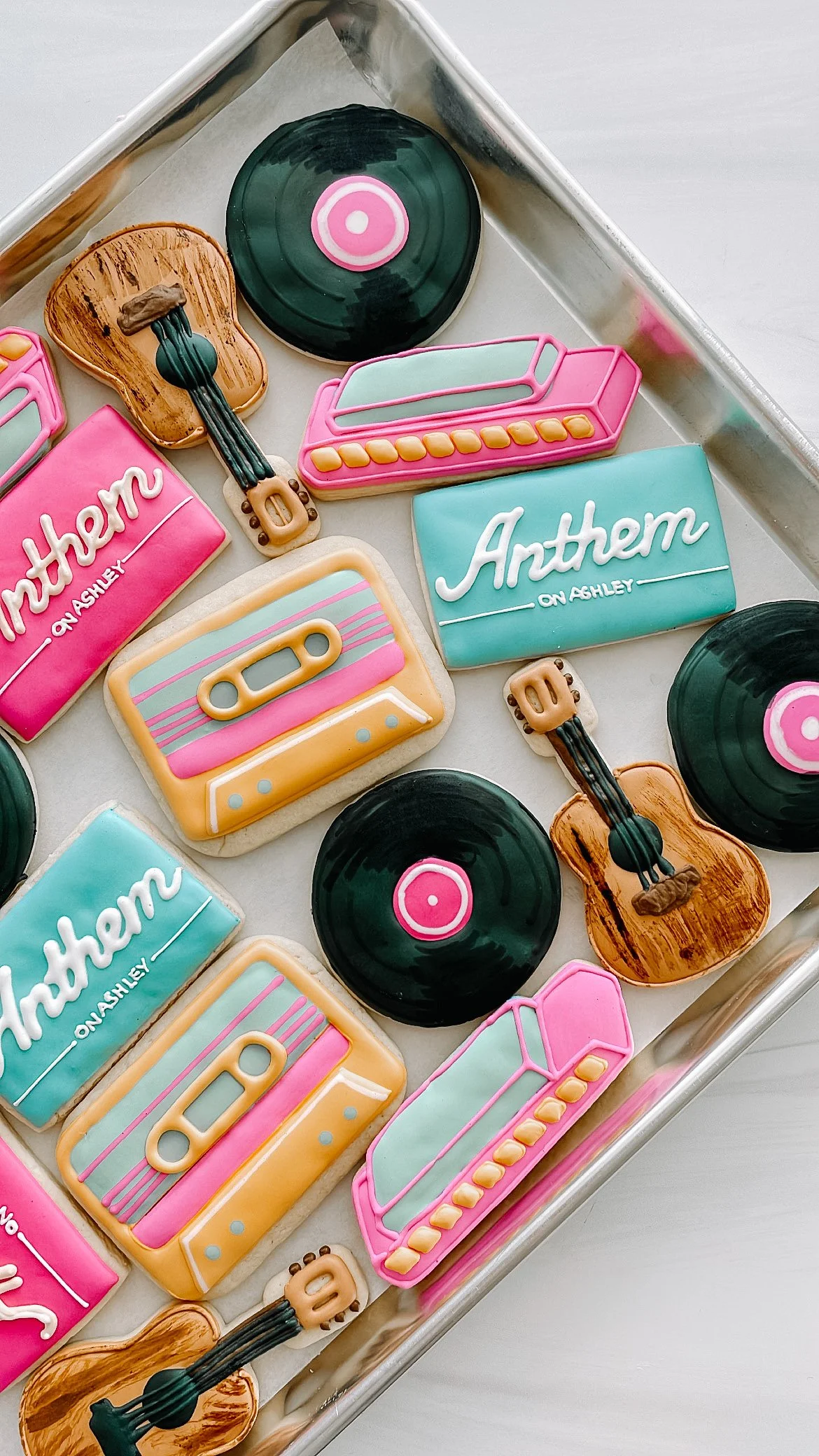 Decorated sugar cookies with pastel pink, teal, yellow, white, and black icing. Designs include an ice cream, vinyl record, guitar, piano, cassette tape, and 