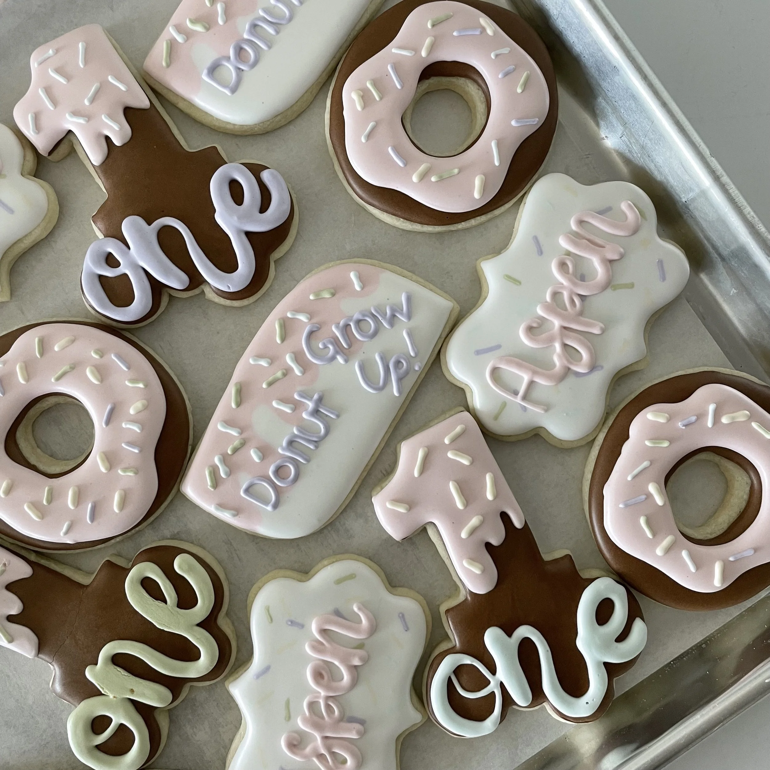 A collection of cookies decorated with various pastel-colored icing, including pink, white, and brown, with sprinkles and writing that says 'Day Off' and 'Yay'.