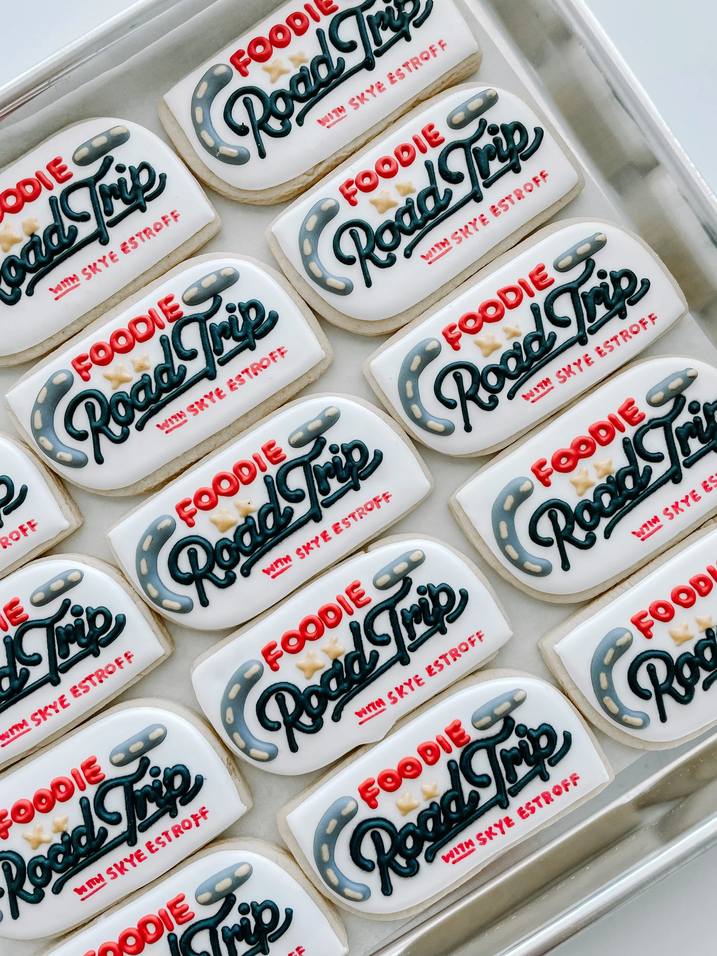 Cookies decorated with a design for the radio show 'Roadside Radio' with Skye Estroff, featuring a white background, text in black and red, a gray steering wheel graphic, and small beige stars.
