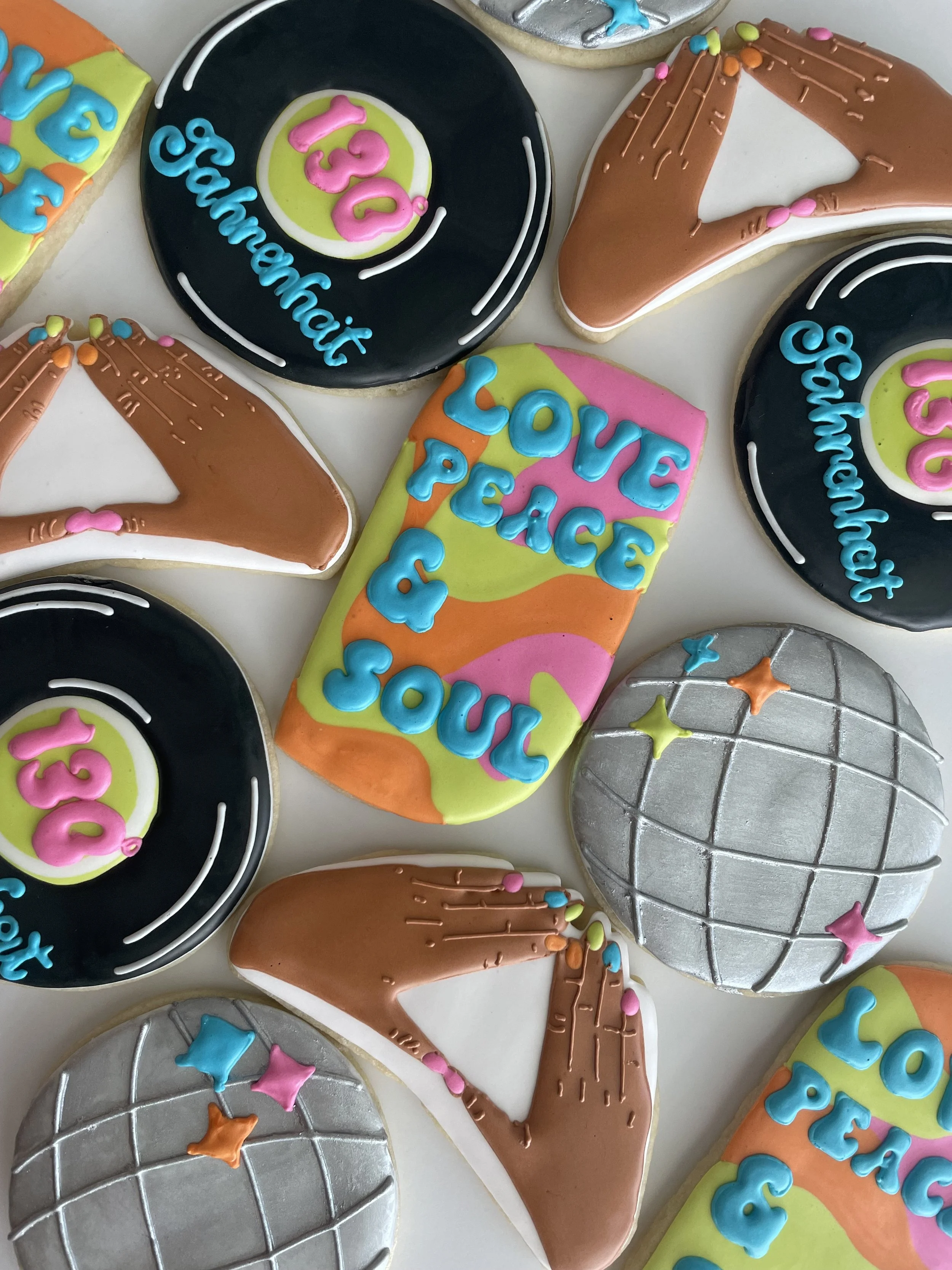 Colorful birthday cookies shaped like records and a hand, decorated with bright icing and messages such as 'Love Peace Soul' and 'Happy 13th Birthday' in pink, blue, orange, and yellow.
