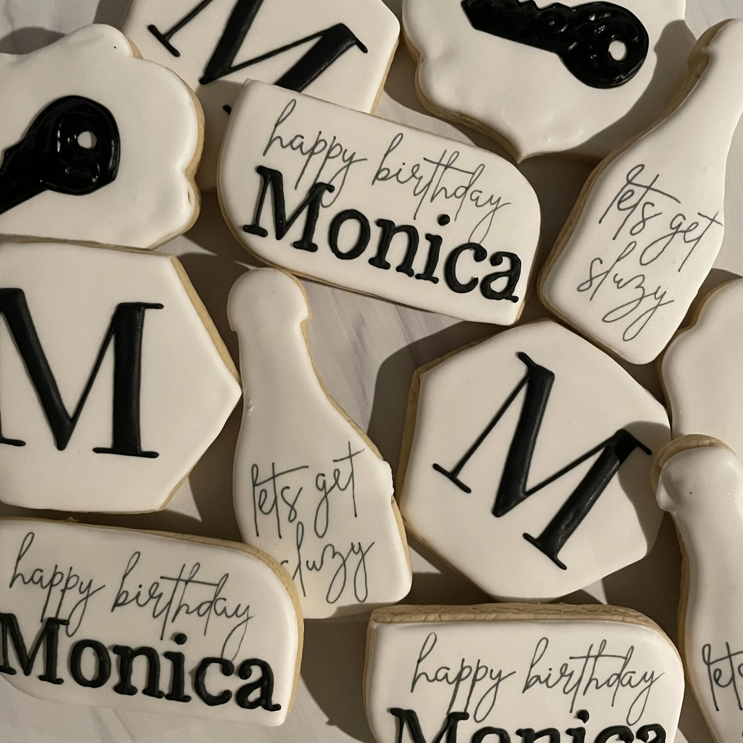 Cookies decorated with black and white icing, some with handwritten cursive messages like 'happy birthday Mom' and 'Let's get', and others with black icing designs.