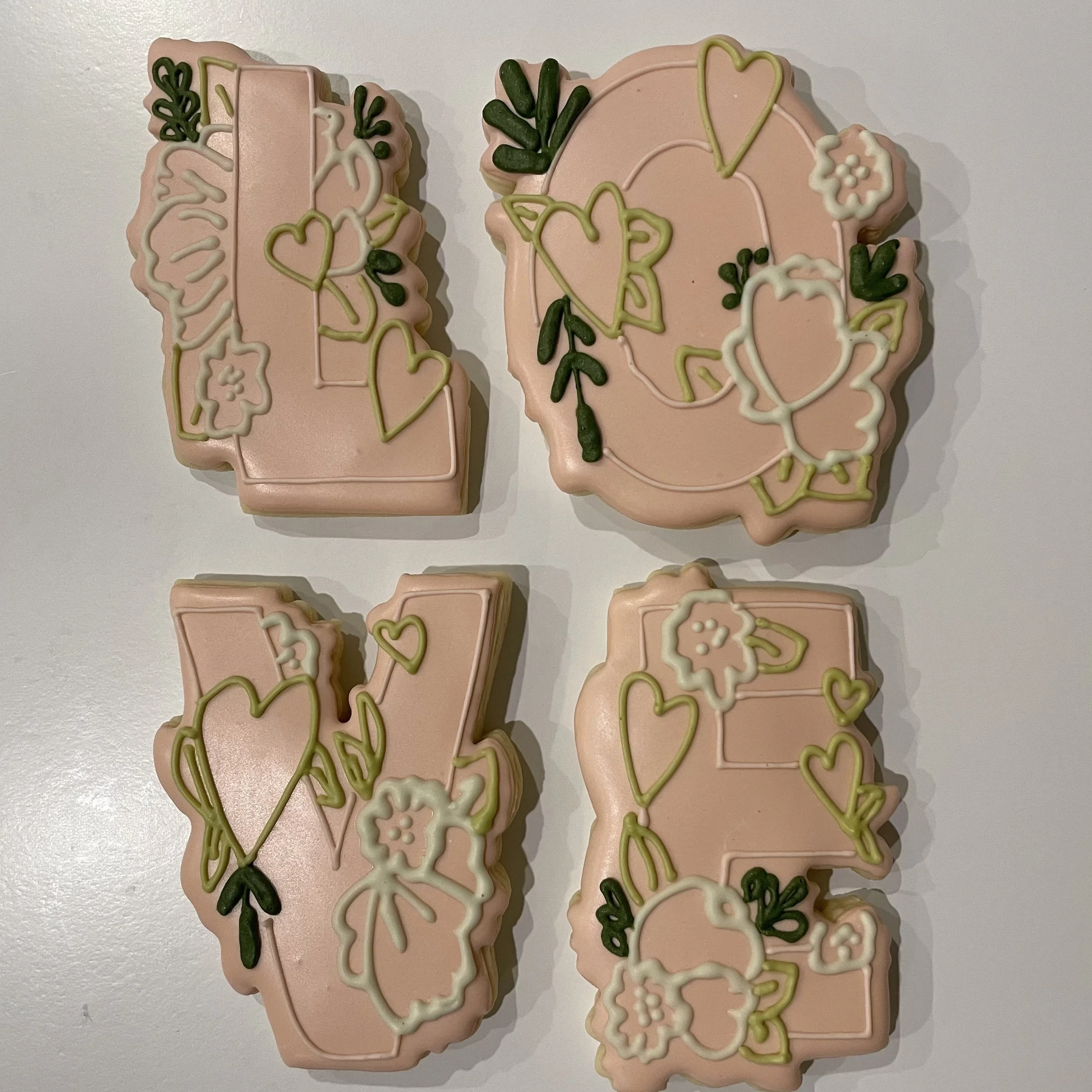 Decorative cookies with pink frosting and green and white icing in the shapes of hearts, leaves, and flowers.
