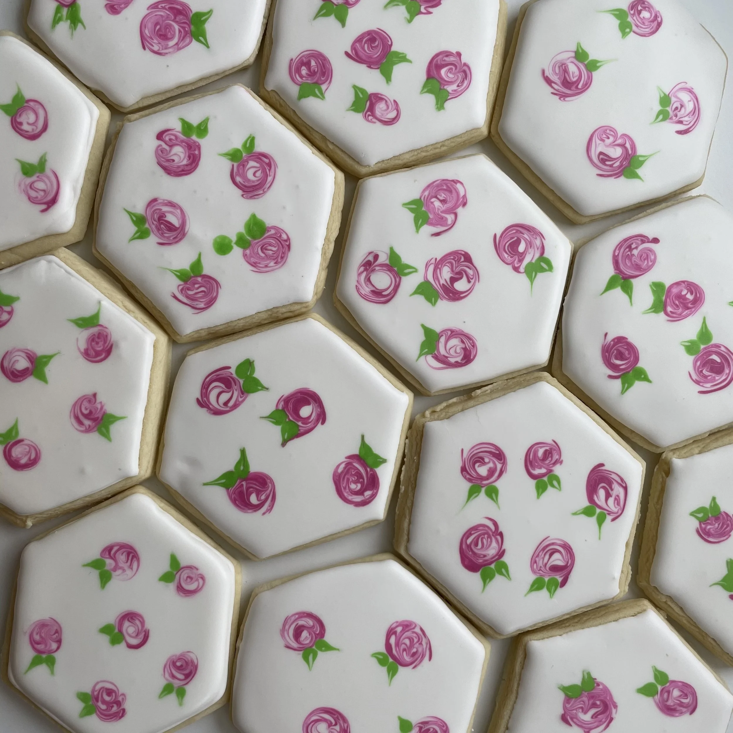 Hexagonal sugar cookies decorated with white icing and pink and green floral designs.