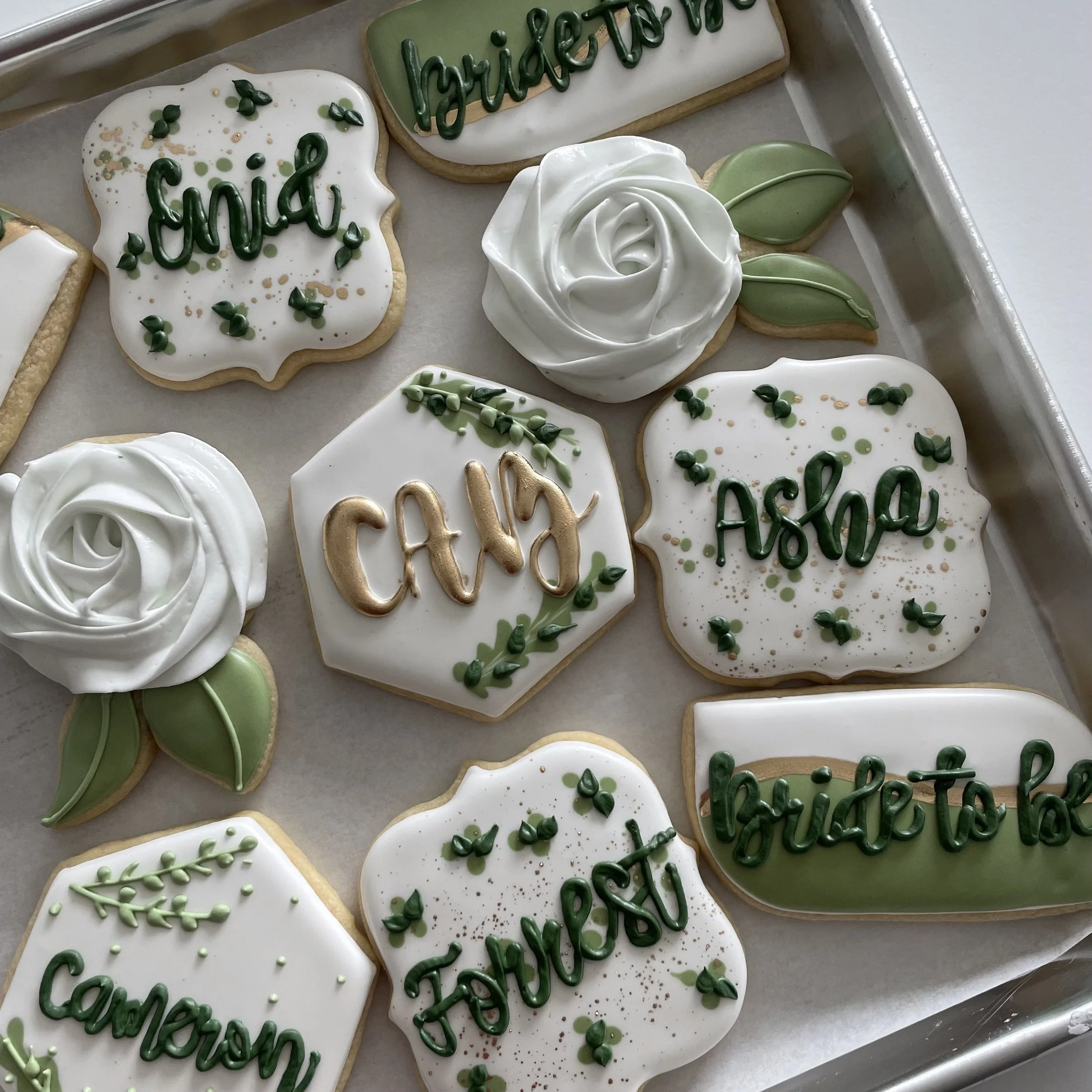 Assorted decorated cookies on a tray, including cookies with green icing spelling 'welcome' and other festive designs.
