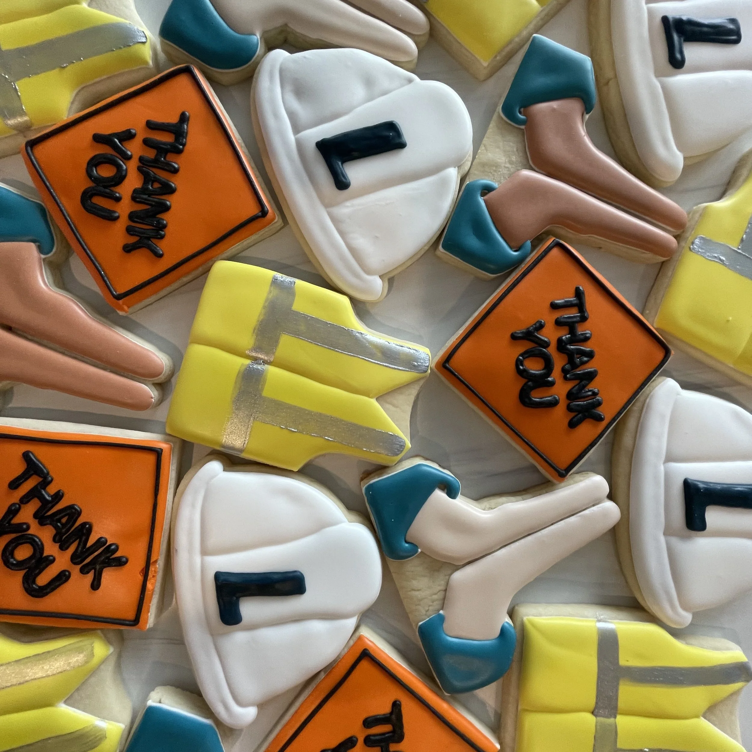 Close-up of decorated cookies with safety symbols, smiley faces, and a sign that says 'Work Happy' in bright colors.