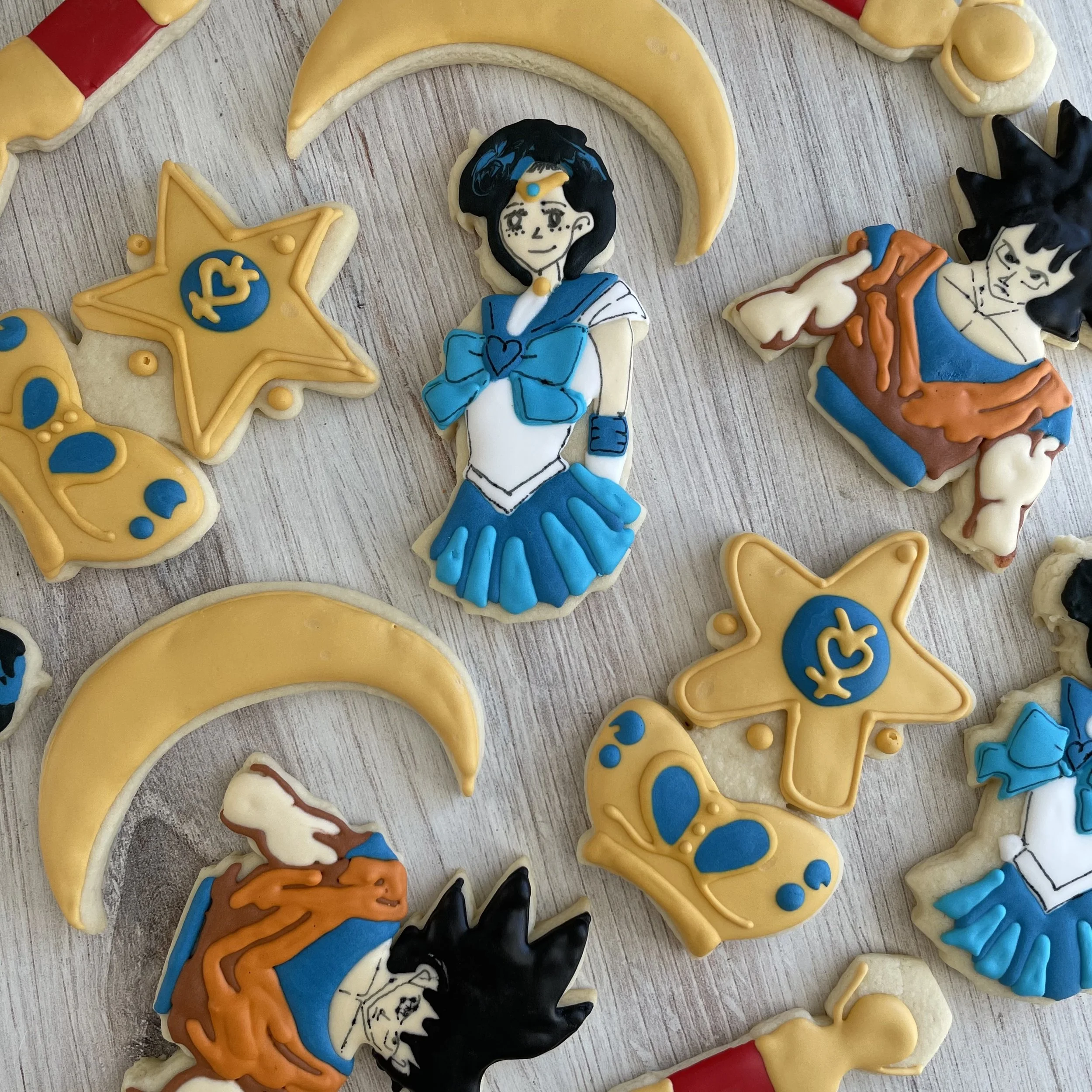 Decorated sugar cookies themed after anime characters, including Sailor Moon, with bright colors like yellow, blue, black, and orange, placed on a wooden surface.